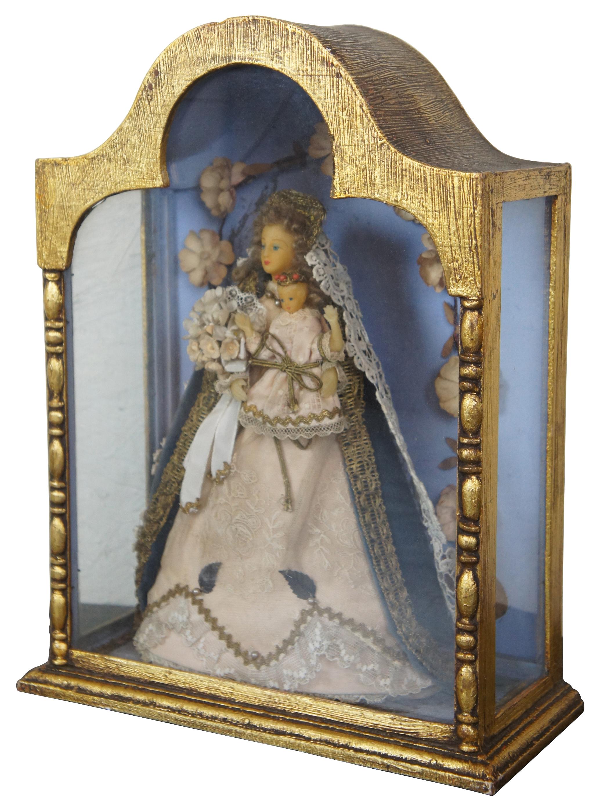 Vintage gilded tabletop display curio shrine case containing the figure of the Virgin Mary dressed as the Queen of Heaven, holding a bouquet of flowers and the Baby Jesus, surrounded by an arch of flowers.
        