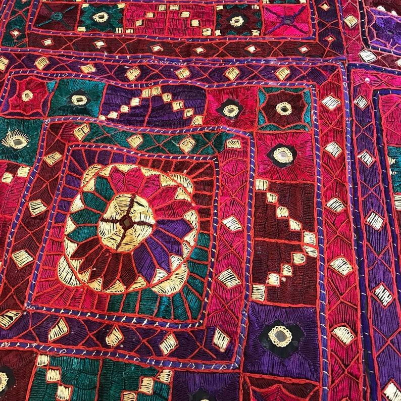 This vibrant, boho-inspired coverlet hails from the Gujarat region of India, featuring dense hand embroidery in rich, colorful silk threads. The captivating floral pattern is accented with intricate mirror work, adding a unique touch of artistry.