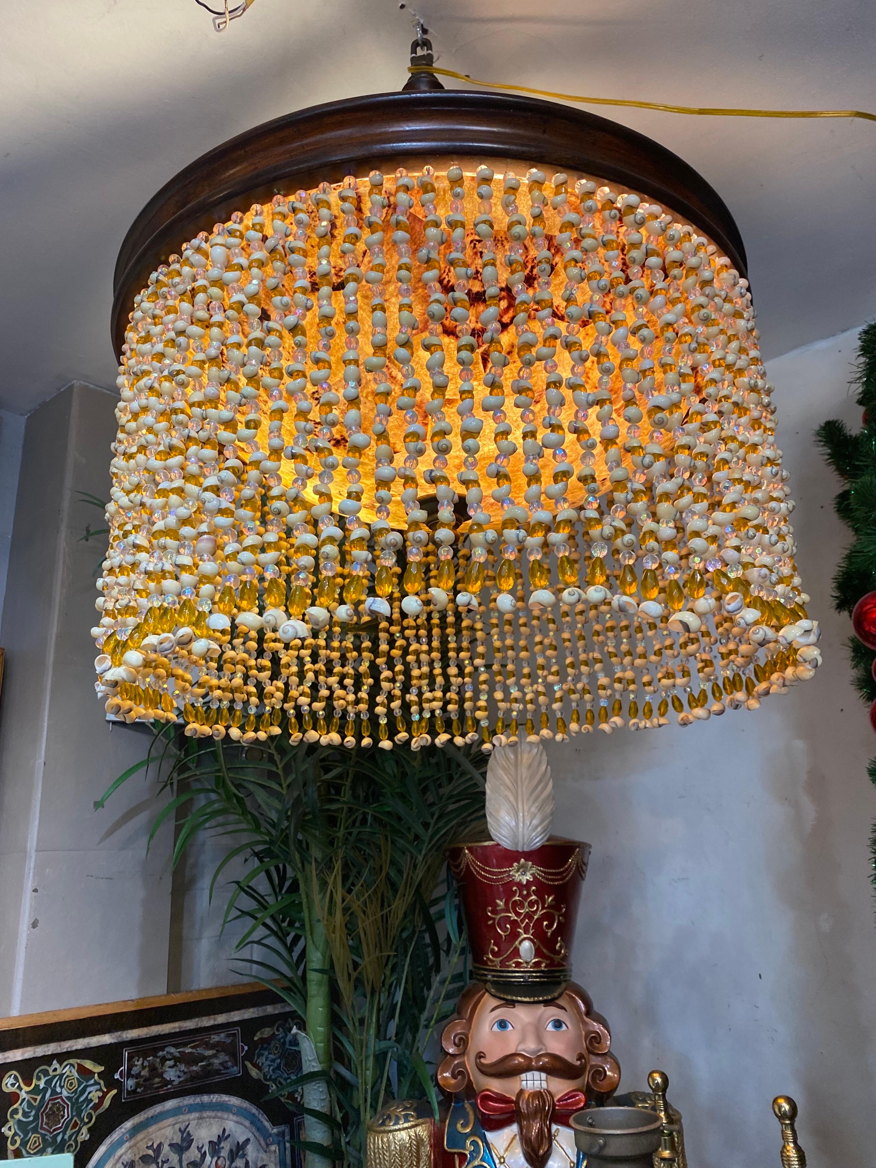 Araña increíblemente escultural hecha con belleza y estilo.  Brillantes cristales y conchas llueven alrededor de una cálida cúpula central en acabado tortuga que cuelga de una escultural base de estilo teca con un resultado así de chic y elegante. 