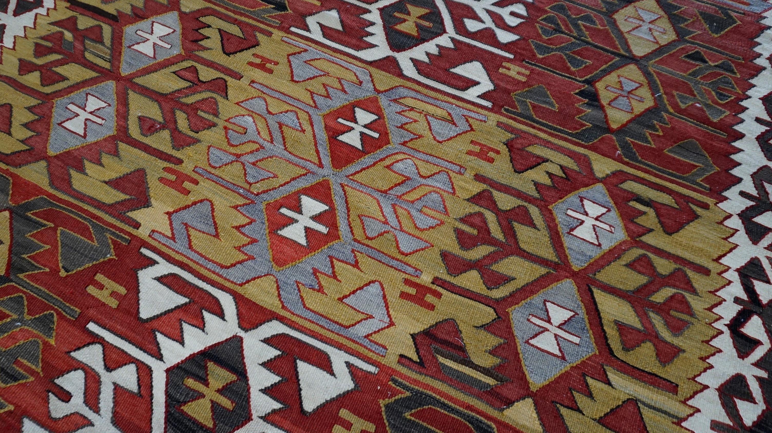 Este llamativo kilim de lana tejida a mano presenta atrevidos motivos geométricos y un fuerte ritmo tribal arraigado en tradiciones de tejido centenarias. Tejida totalmente a mano con la técnica del tejido plano, la alfombra muestra una secuencia