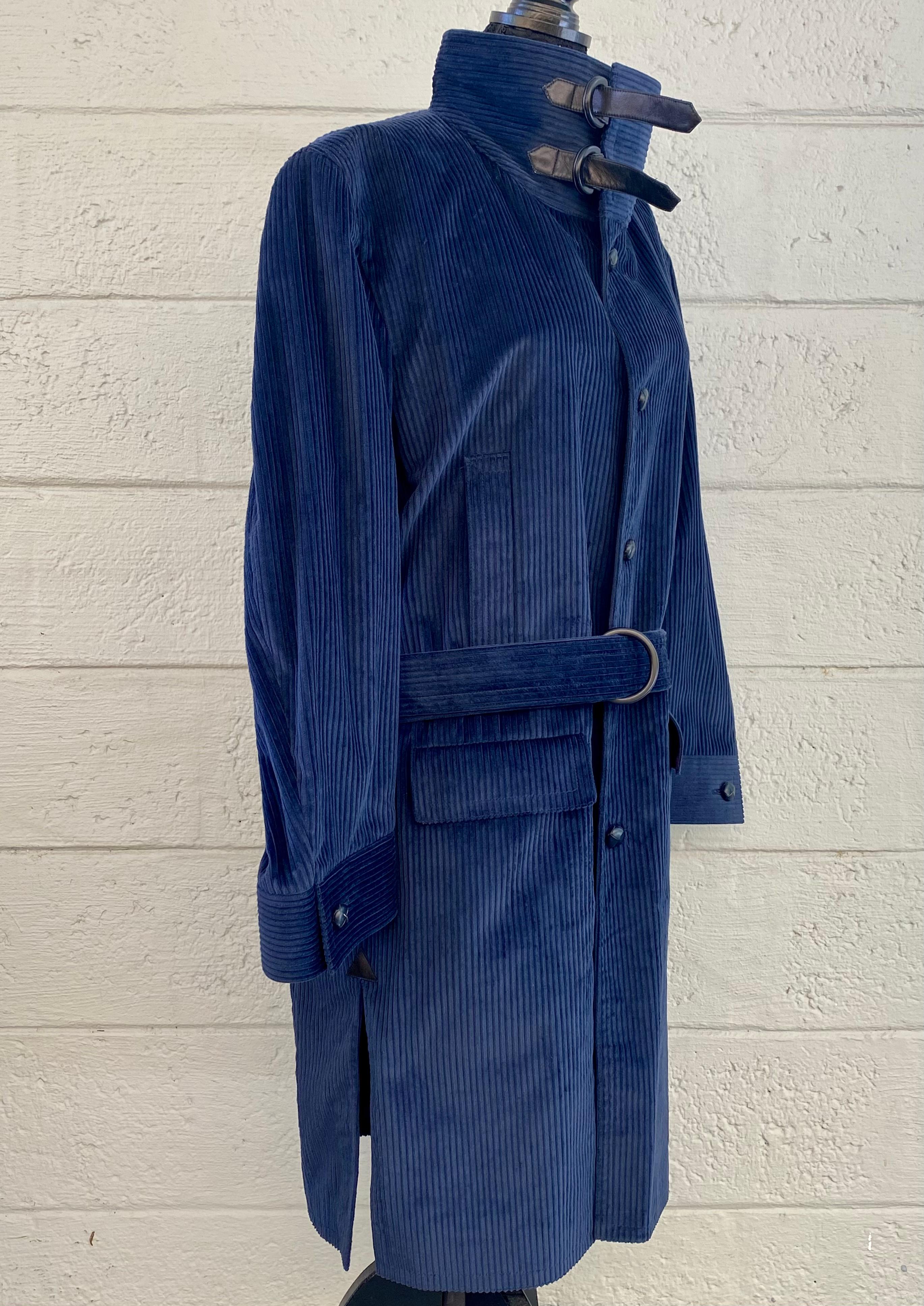Magnifique trench-coat classique Pierre Cardin Boutique, datant de 1980. Fabriqué en France. Le velours côtelé bleu marine présente le traditionnel rabat-tempête, la taille à nouer et une grande fente dans le dos. Cela contraste avec les styles