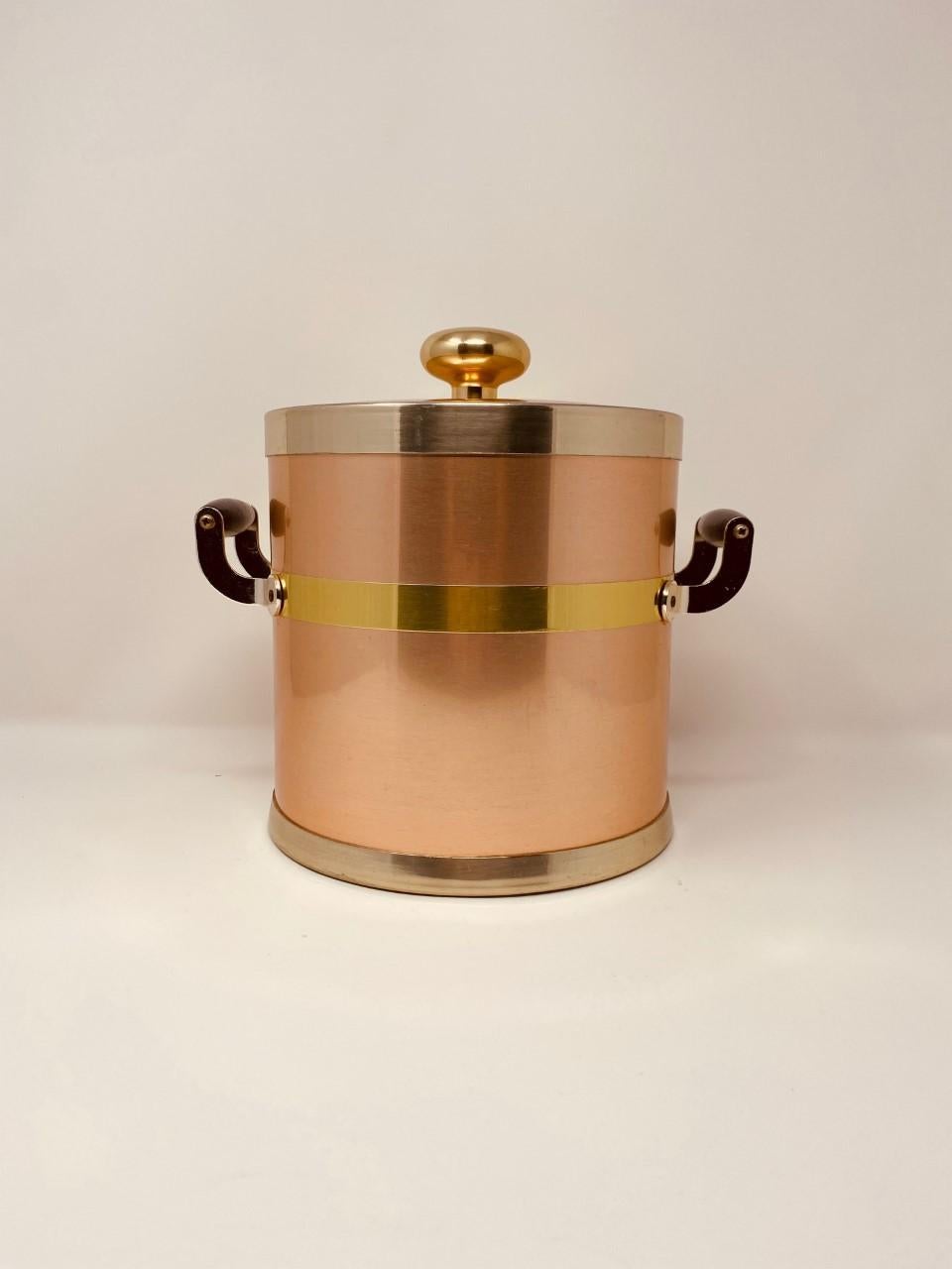 Glamorous and elegant vintage copper ice bucket. This 1950s beautiful midcentury piece is rare and special because of its color that hints on a rose tone of copper. The piece is streamlined and is accented with gold metal edges and dark wood handles
