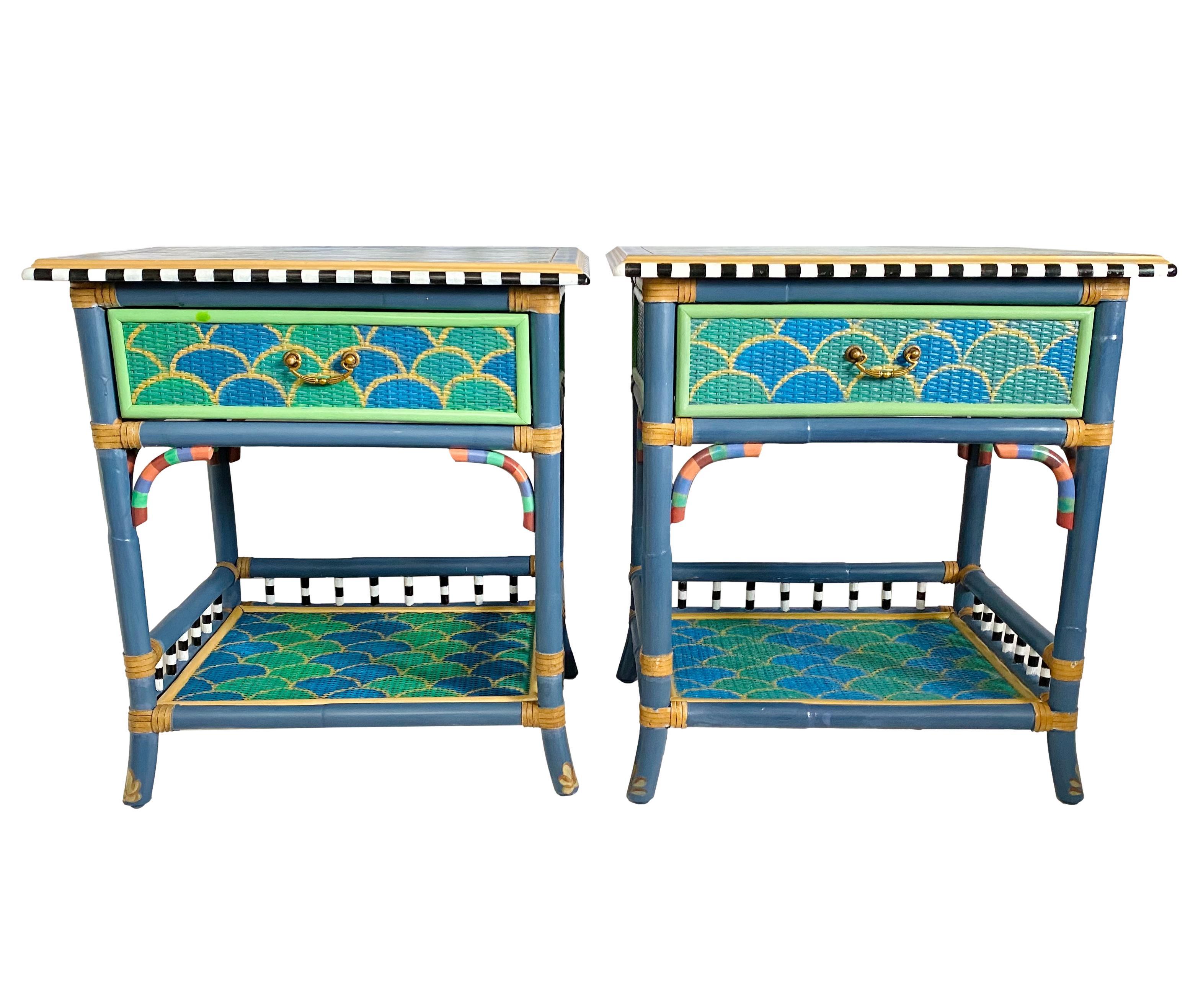 A vintage pair of single-drawer side tables or nightstands hand-painted in the style of MacKenzie-Childs Madras collection. Featuring ogee, tartan, and check patterns in blues, greens, gold, coral, black & white. 

Rattan frames with leather