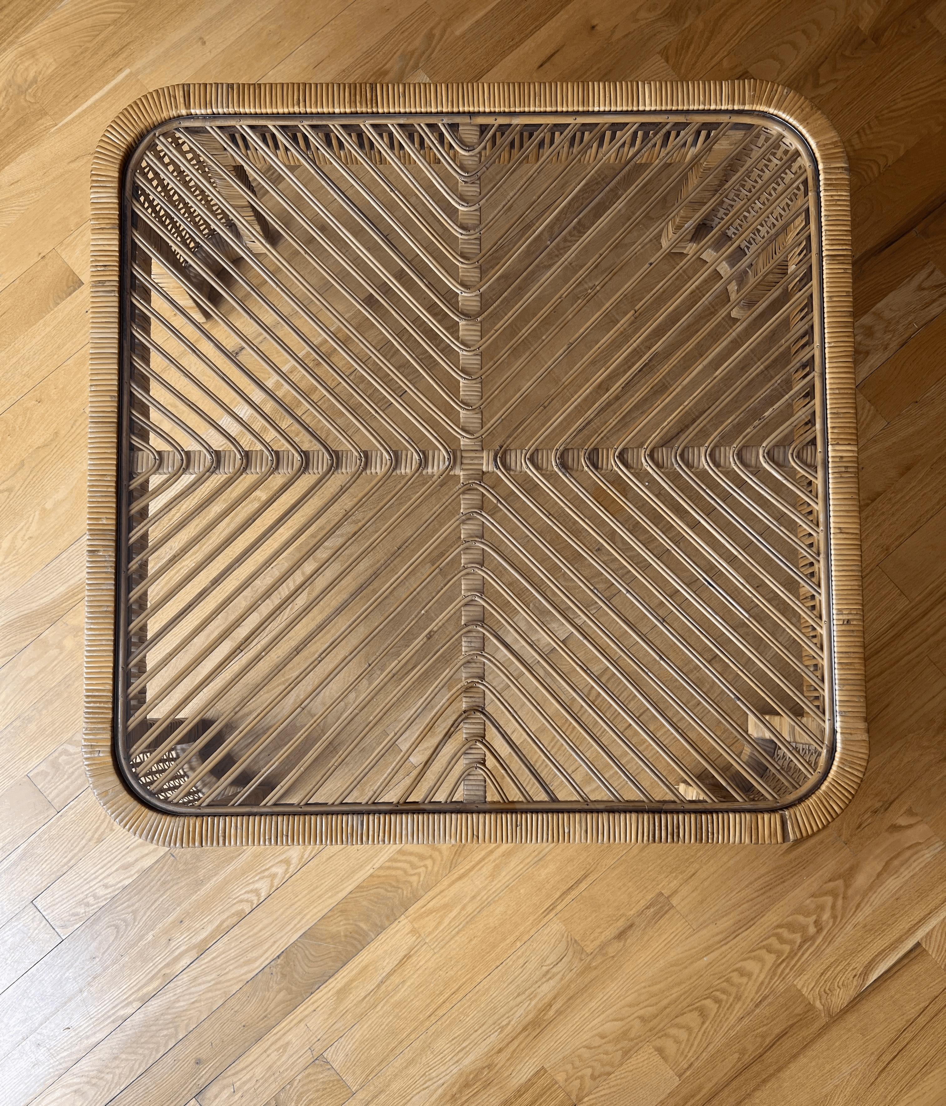A bold and sculptural vintage rattan and bamboo coffee table featuring a square form with softly rounded corners and curved legs. The woven base is topped with a removable glass insert that reveals an eye-catching chevron pattern formed by