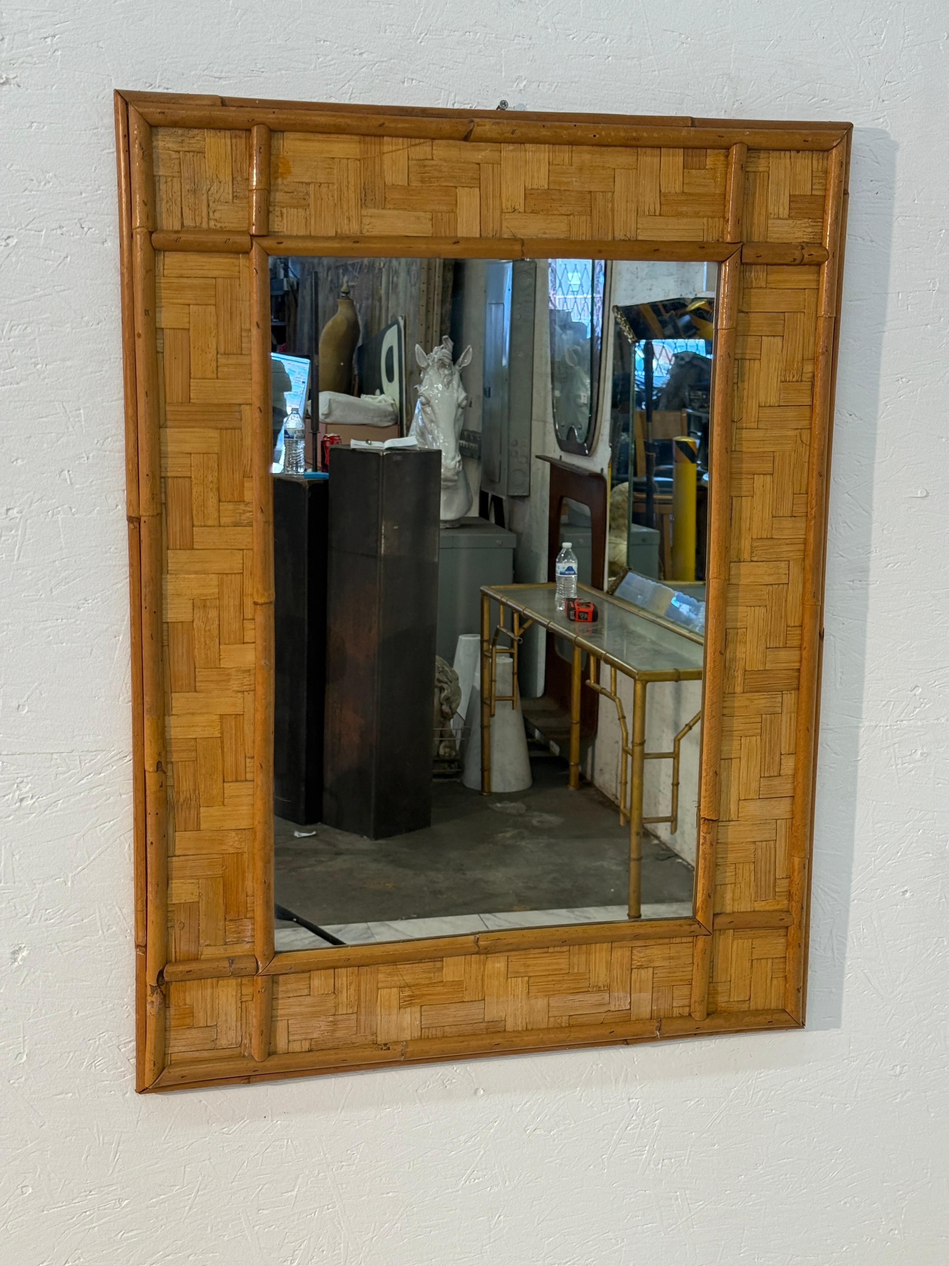 Un charmant miroir mural rectangulaire encadré de rotin tressé avec des accents de bambou. Le design met en valeur un motif d'incrustation en rotin tressé en panier, entouré de tiges de bambou arrondies qui ajoutent de la texture et de la