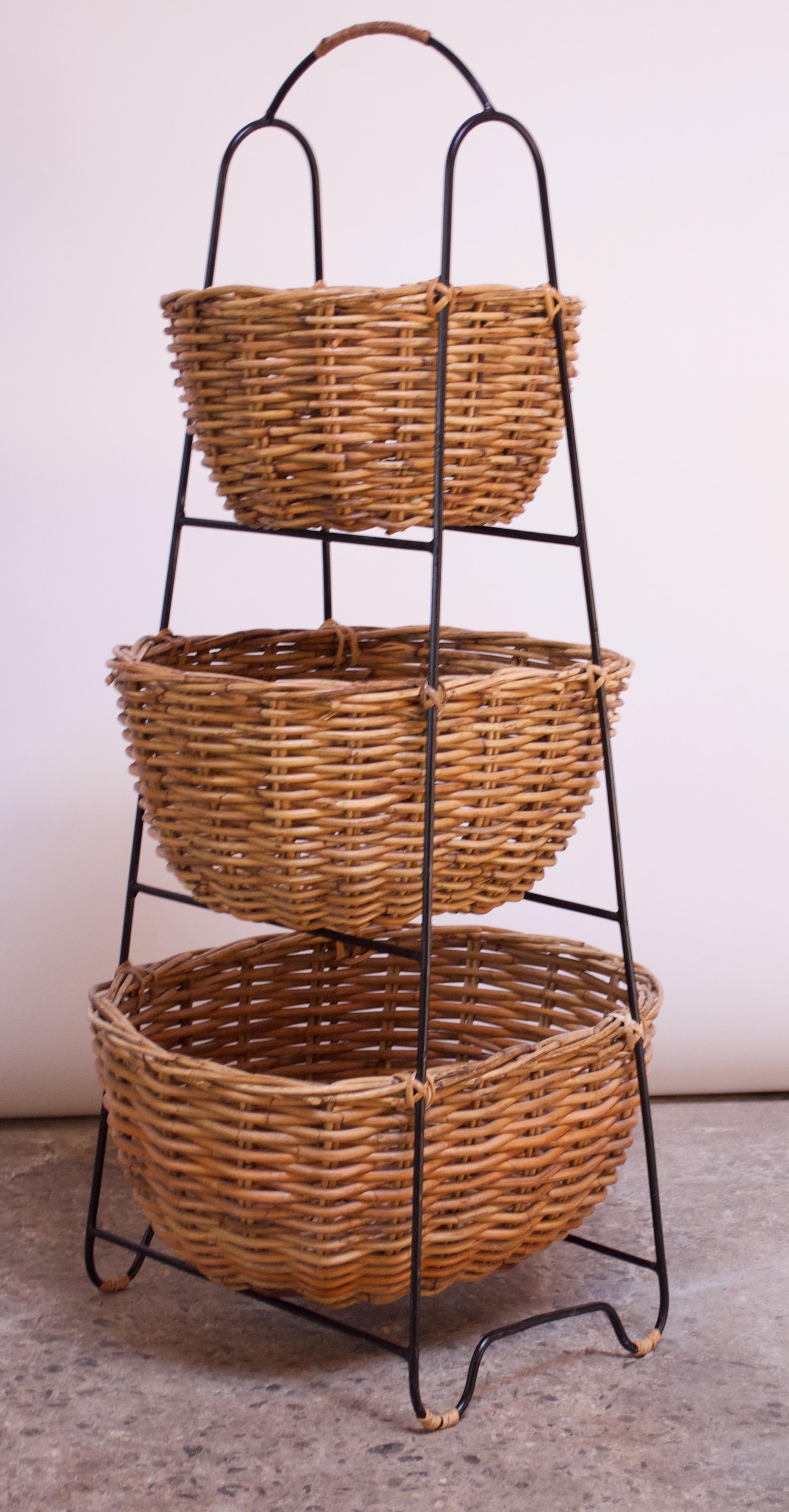 Unique vintage storage stand composed of three cane-baskets in varying sizes mounted to a wrought iron stand. Handle is wrapped in a warm-hued rattan, and rattan 'ties' attach the baskets to the iron frame. Reminiscent of designs by Arthur Umanoff,