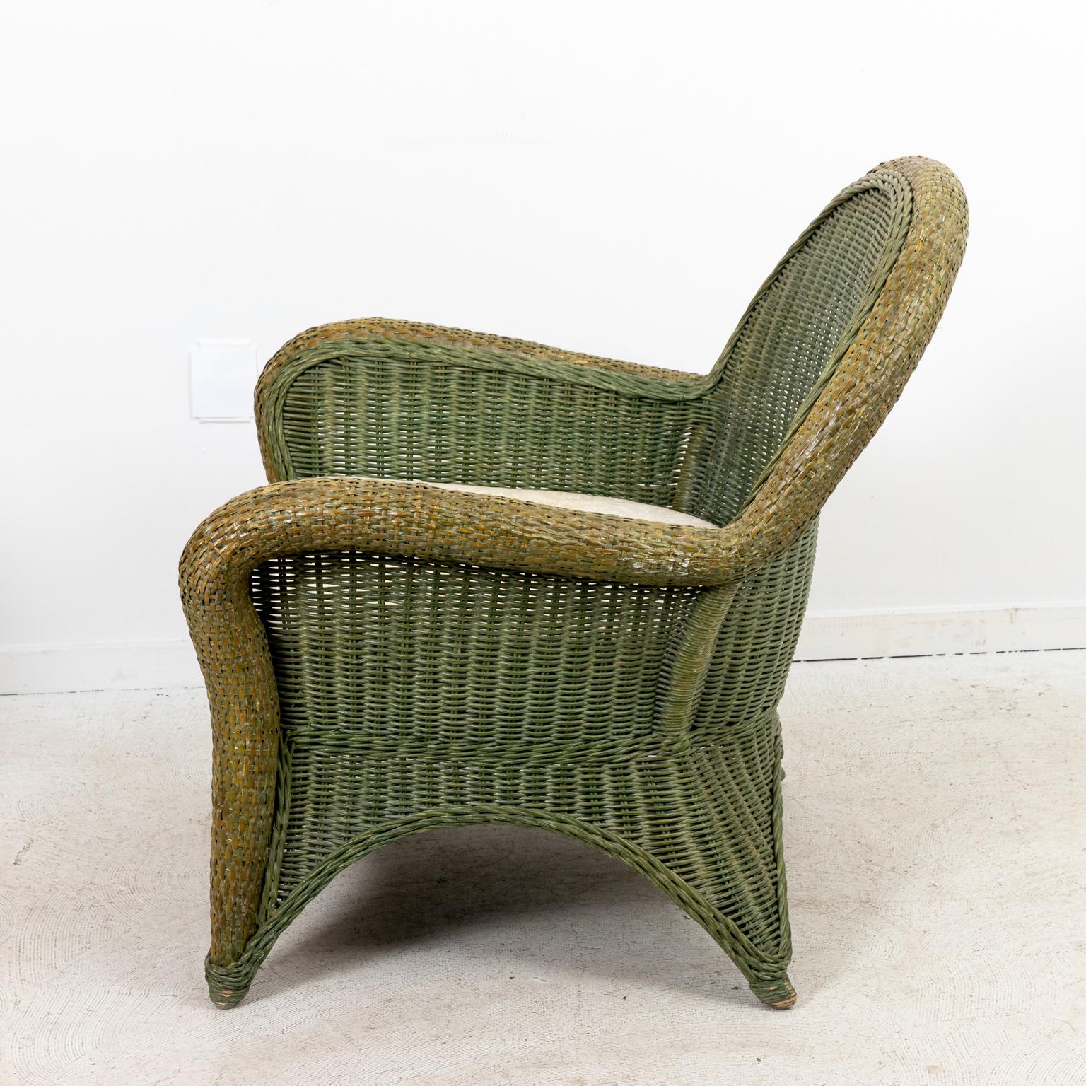 Vintage painted rattan armchair with white cotton upholstered seat cushion. The piece is painted overall in a shade of green with braided side trim which adds an unusual detail. The arched back also features a cross hatch design. Made in the United