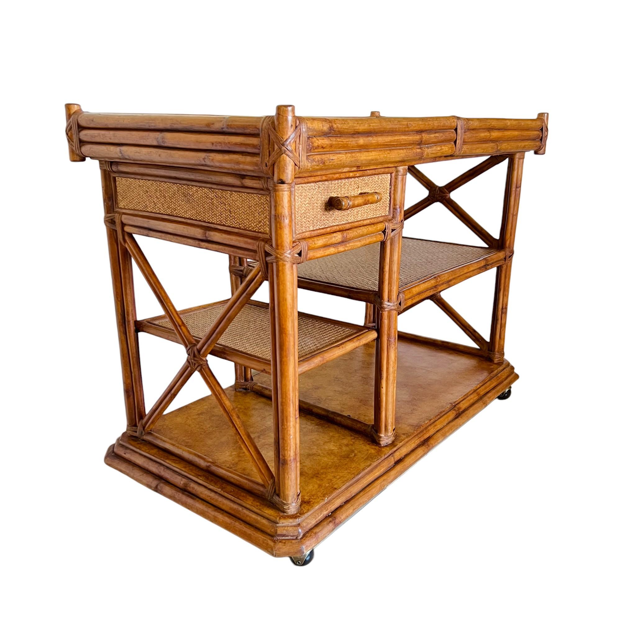 A vintage 1970's Palm Beach Regency rolling bar cart or server with extending top. Rattan framing with woven reed top surface, shelves, drawer face and side/back panels. This versatile piece features an expanding top that slides out to reveal a