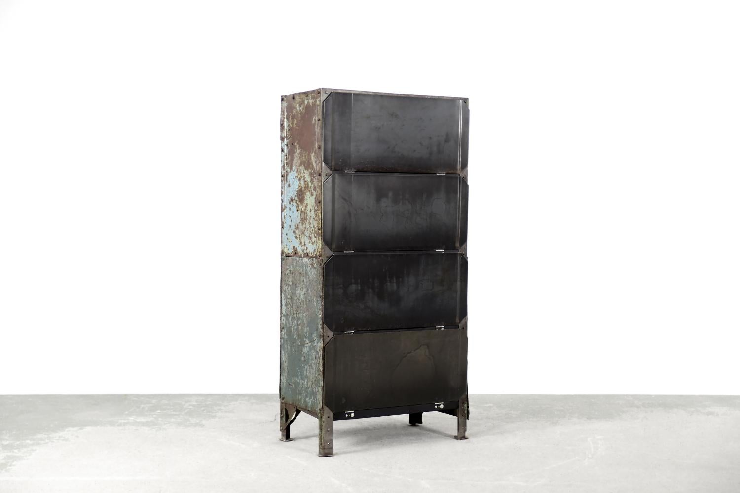 This industrial factory cabinet was produced during the 1950s. It is made of metal. It has four shelves closed with a magnetic latch. All shelves has been cleaned and finished in black inside. The original layers of varnishes, paints and tarnish
