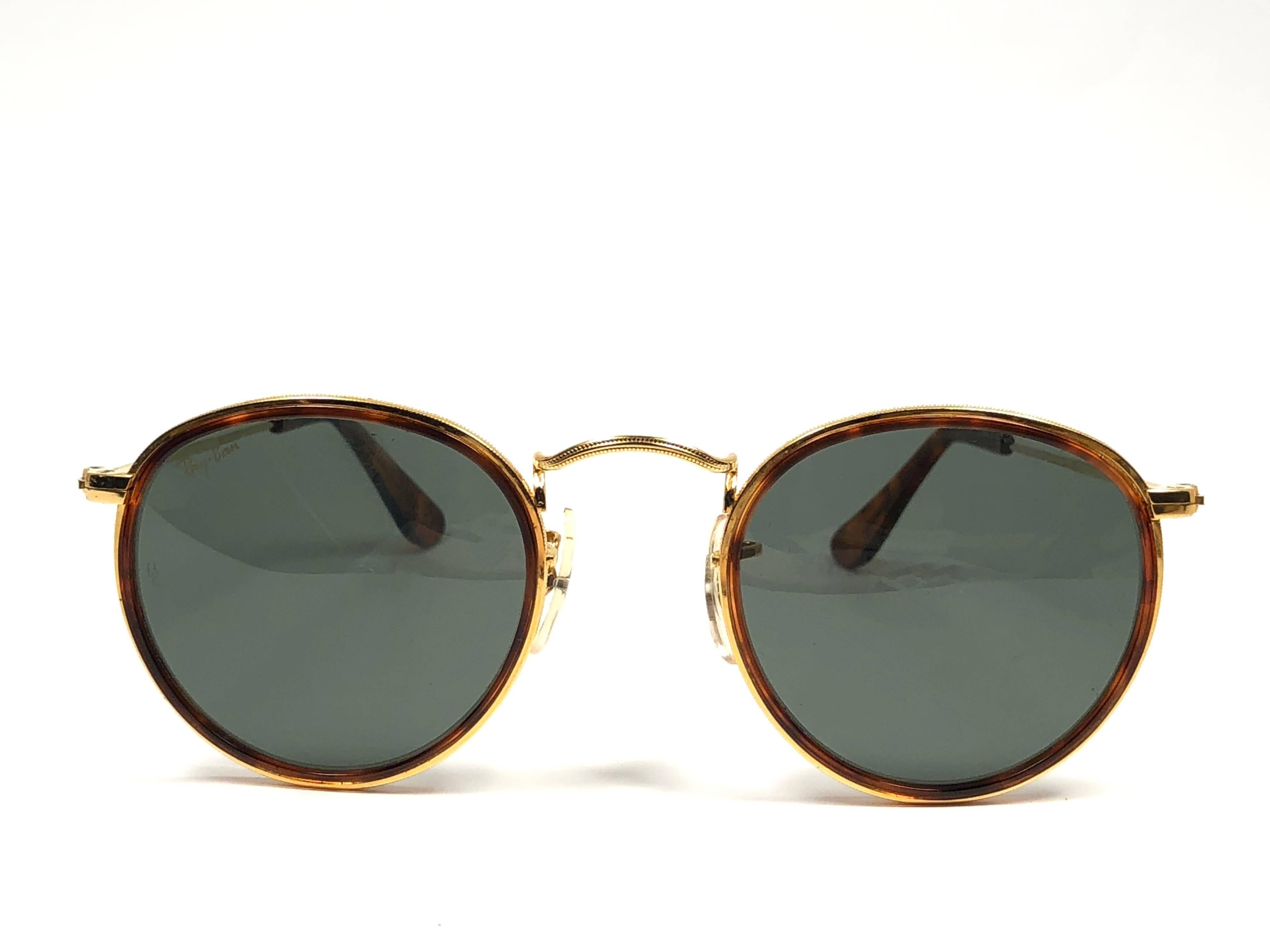 New Vintage Ray Ban classic round frame with tortoise inserts sporting G15 grey lenses.
Comes with its original Ray Ban B&L case with minor sign of wear due to storage.  

FRONT : 12.5 CMS
LENS HEIGHT : 4.6 CMS
LENS WIDTH :4.8 CMS

