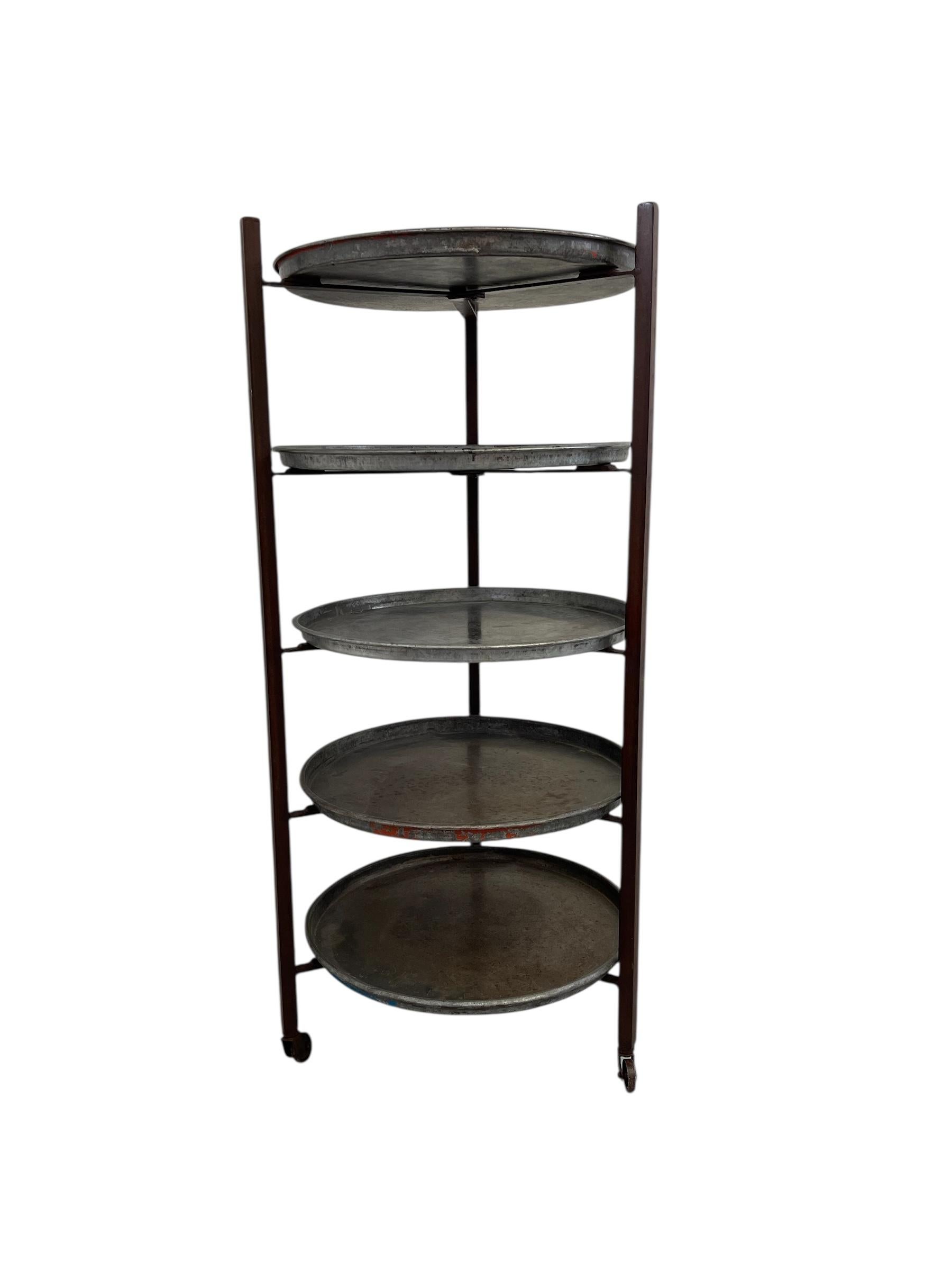 This vintage bakery shelf rack features round galvanized metal trays supported by a rust-finished iron frame. Each tray is removable and sits in a custom notched bracket that allows it to tilt or lift out entirely, offering versatile display or