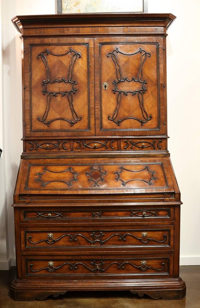 Fantastic Italian walnut secretary made from reclaimed wood, featuring raised carved details on front, doors and drawers. Has a drop down writing surface with small covered drawers throughout. Brass accents of Lion's Head handles adorn the drawers