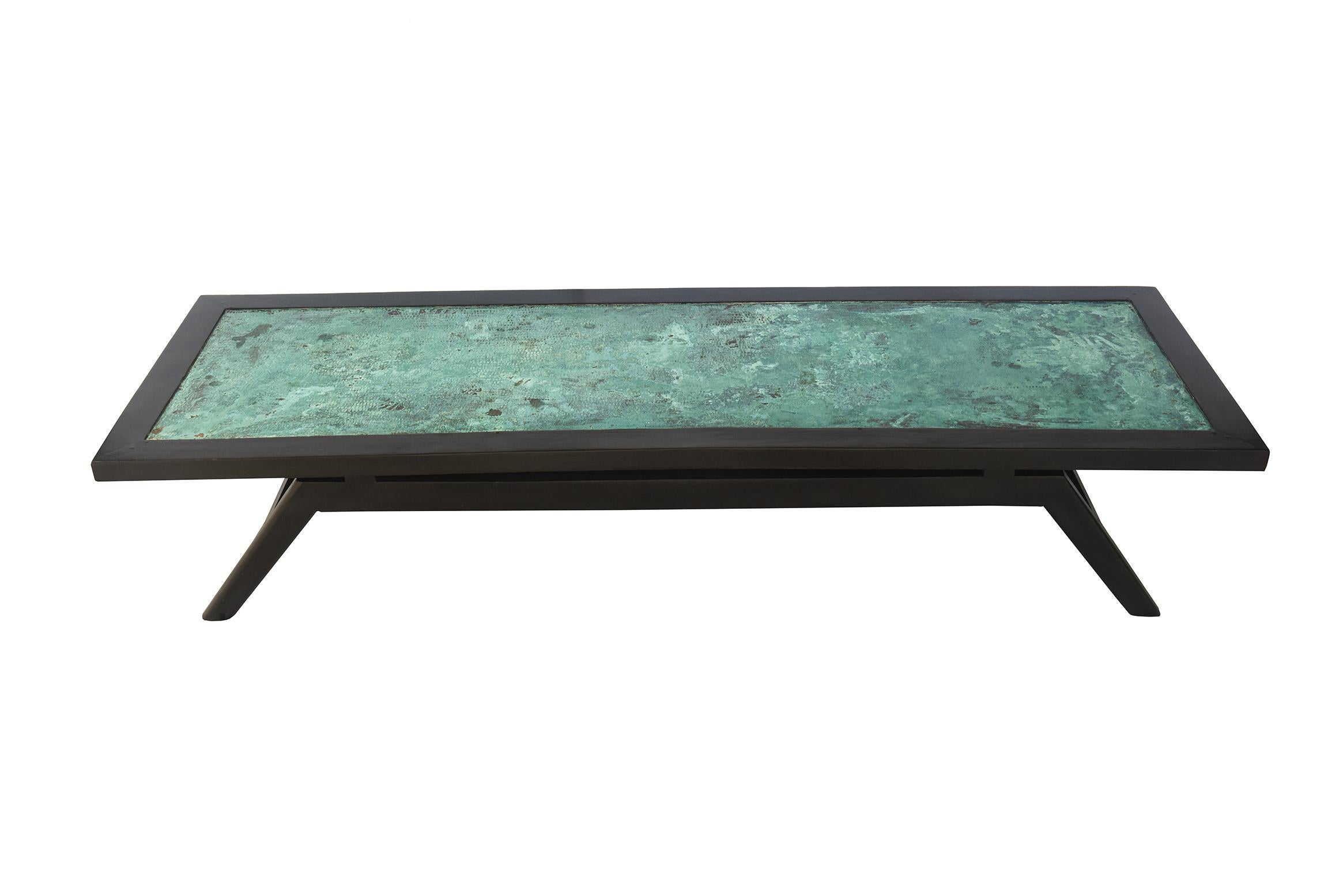 This vintage elongated rectangular cocktail table is black stained oak with an artistic top of patinated hammered copper that results in mottled turquoise and green colors with tan brown peaking through. It is both modern and has rustic qualities