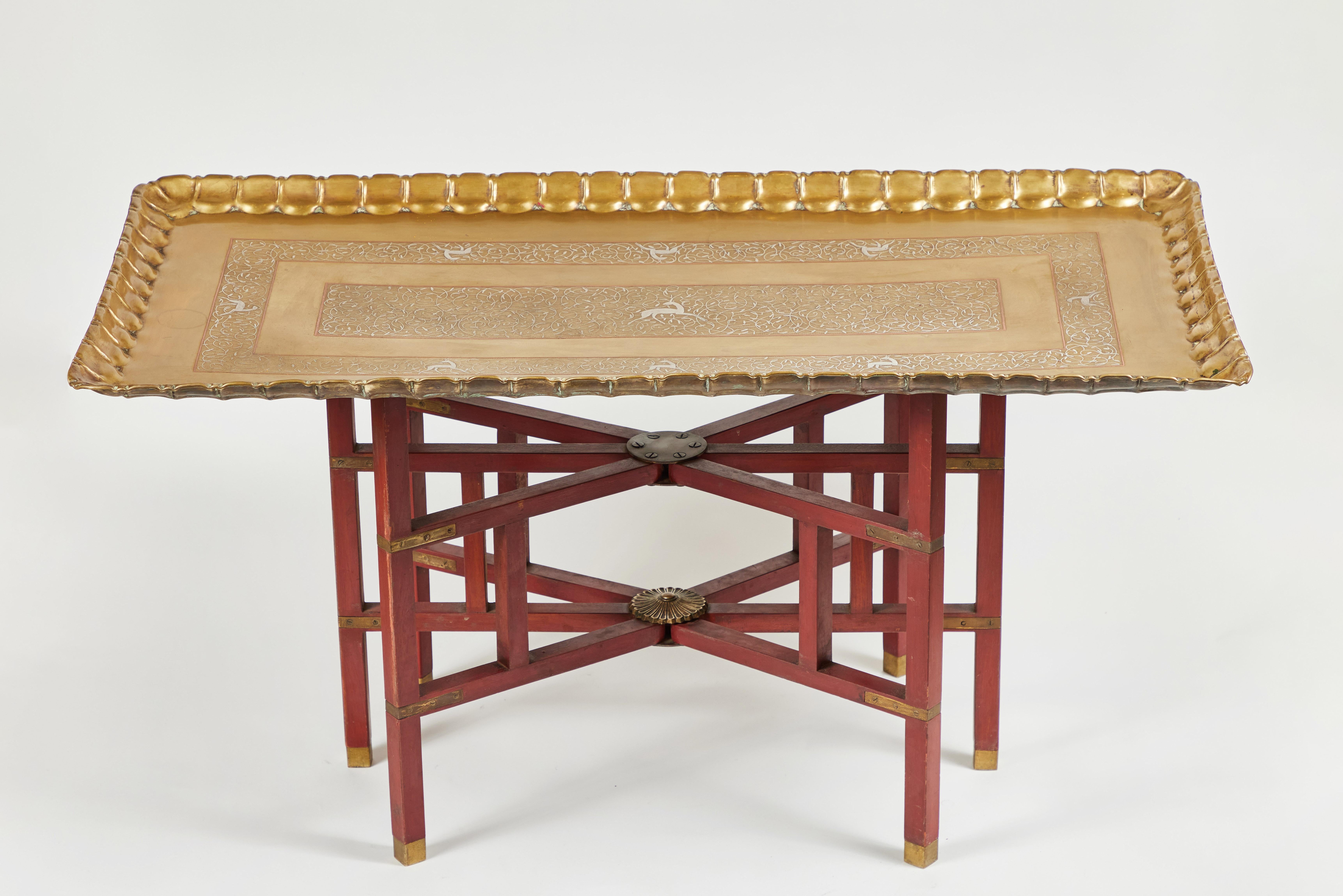 This outstanding vintage rectangular brass tray table sits on a complimentary red collapsible base.
The tray has a gorgeous Inlay motif of copper and silver with a decorative fluted edge. The wood base has a worn red finish and bold brass fittings.