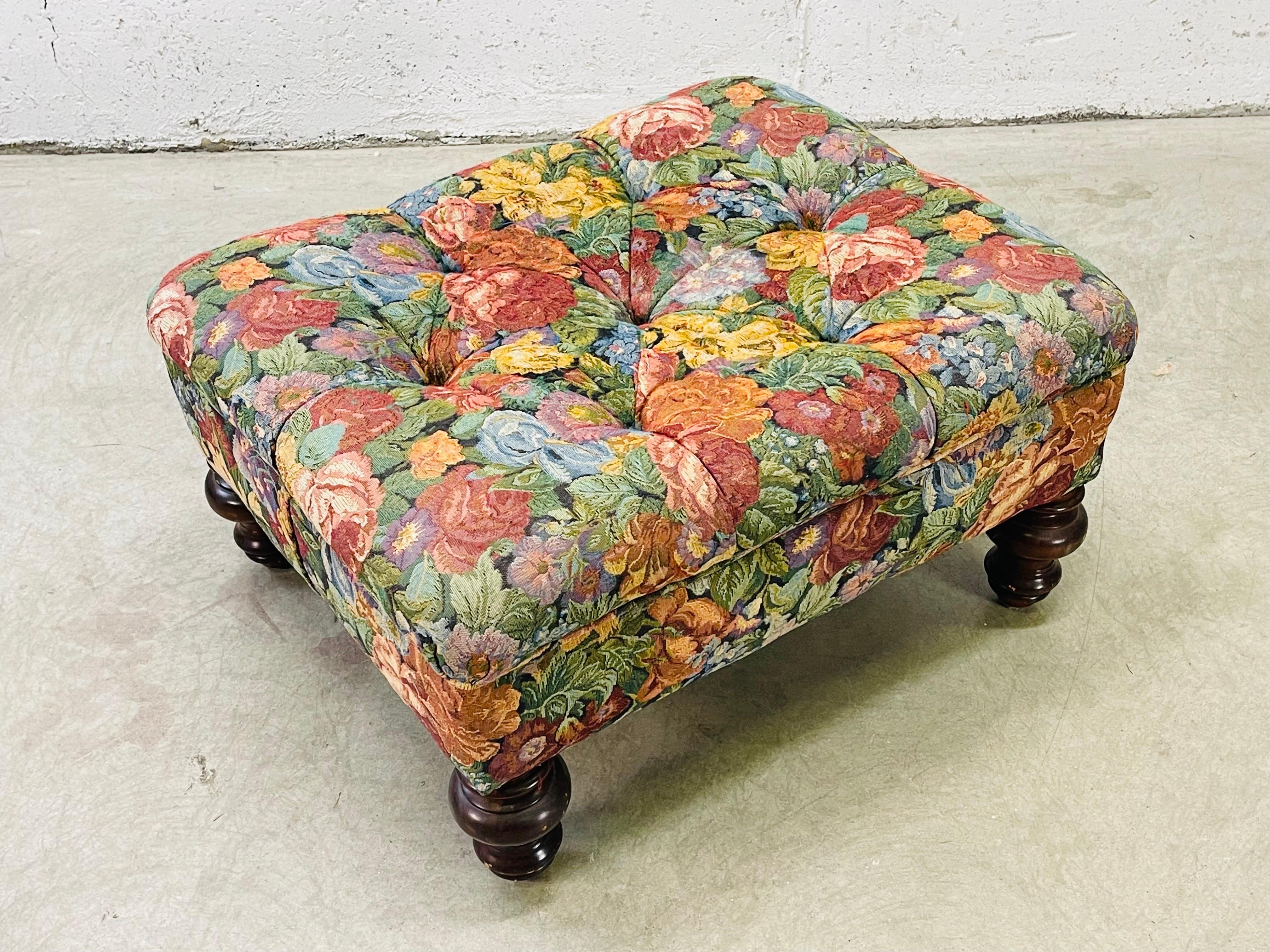 Vintage 1980s rectangular tufted ottoman with round wood legs. The ottoman has a floral fabric that needs to be replaced. The ottoman is solid and sturdy. No marks.