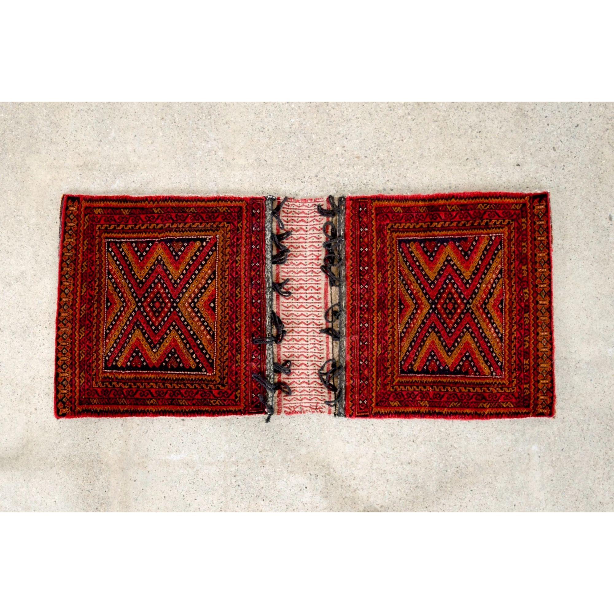 This authentic vintage Baluch tribal saddlebag rug is from a region near present-day Afghanistan and Pakistan. This small expertly handcrafted rug is connected by flat woven kilim with suspension loops and features an intricate geometric tribal