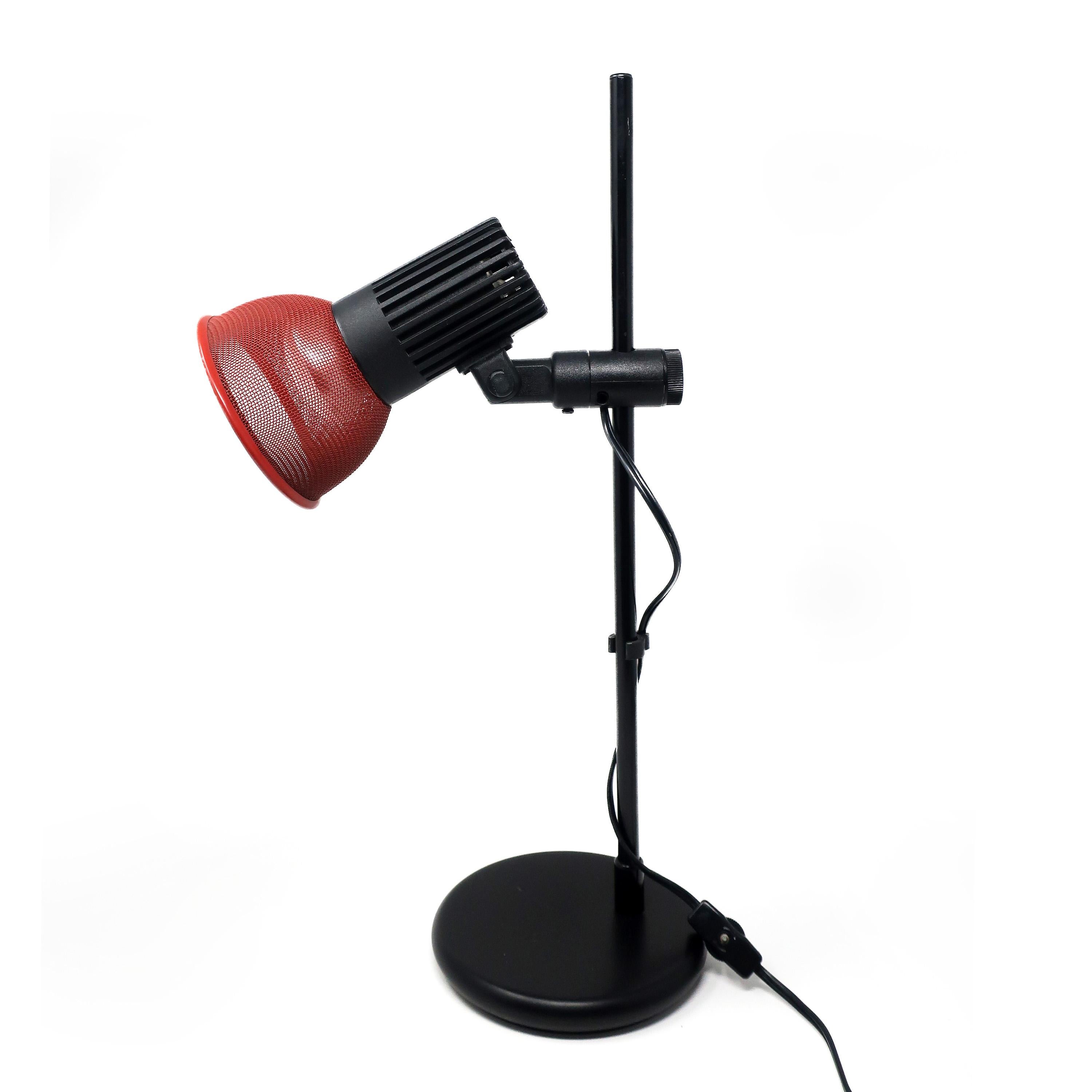Eine auffällige verstellbare Schreibtischlampe aus den 1980er Jahren mit rundem, schwarz emailliertem Sockel und Stiel, rotem Metallschirm und Schalter am Kabel. Höhe und Winkel sind einstellbar, ebenso wie die Kordelklammern. 

In sehr gutem