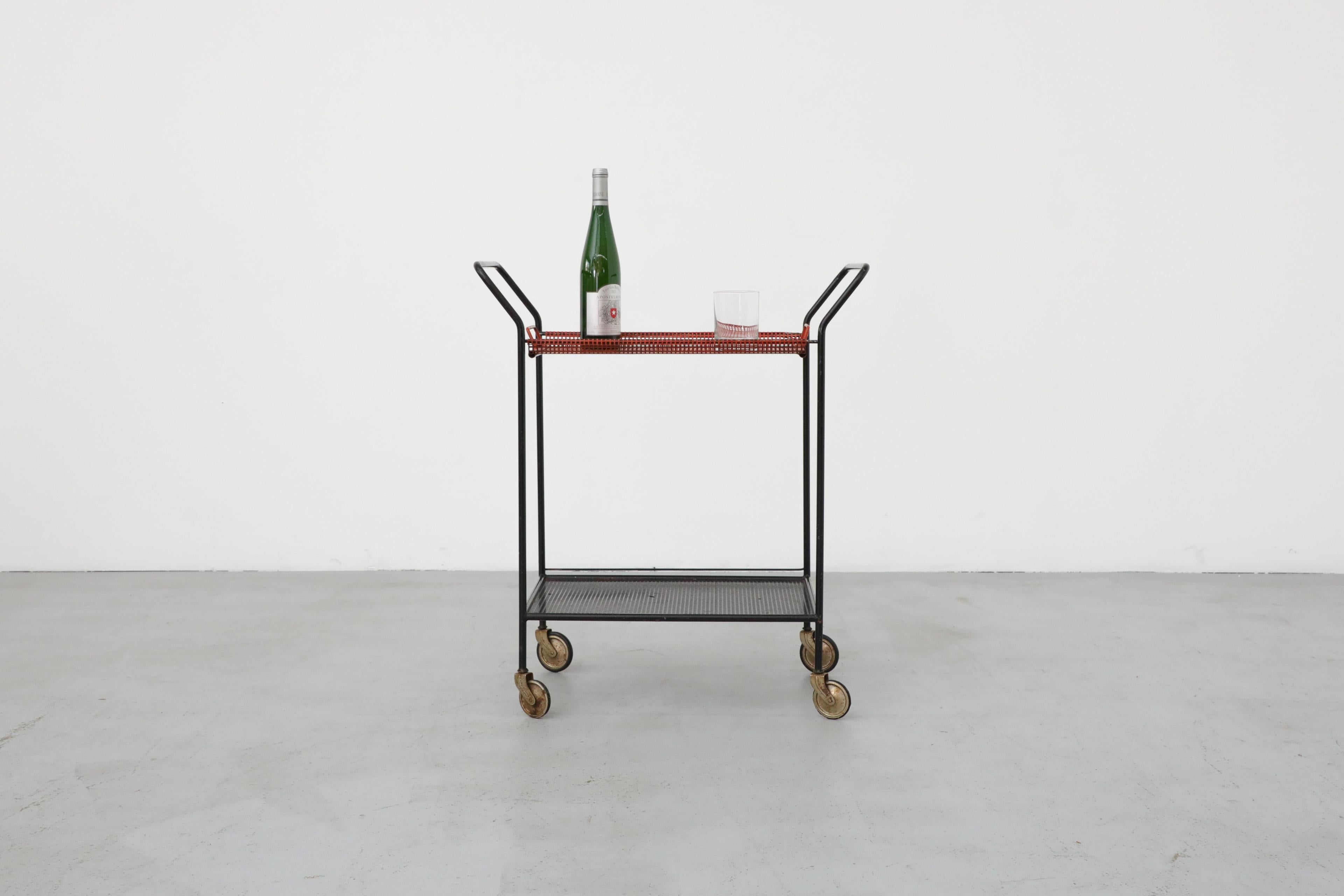 Vintage Pilastro rolling bar cart or tea trolley with perforated red removable top tray and black perforated lower shelf, black enameled metal frame, brass wheels and towel holder. In original condition with visible wear, including chips and
