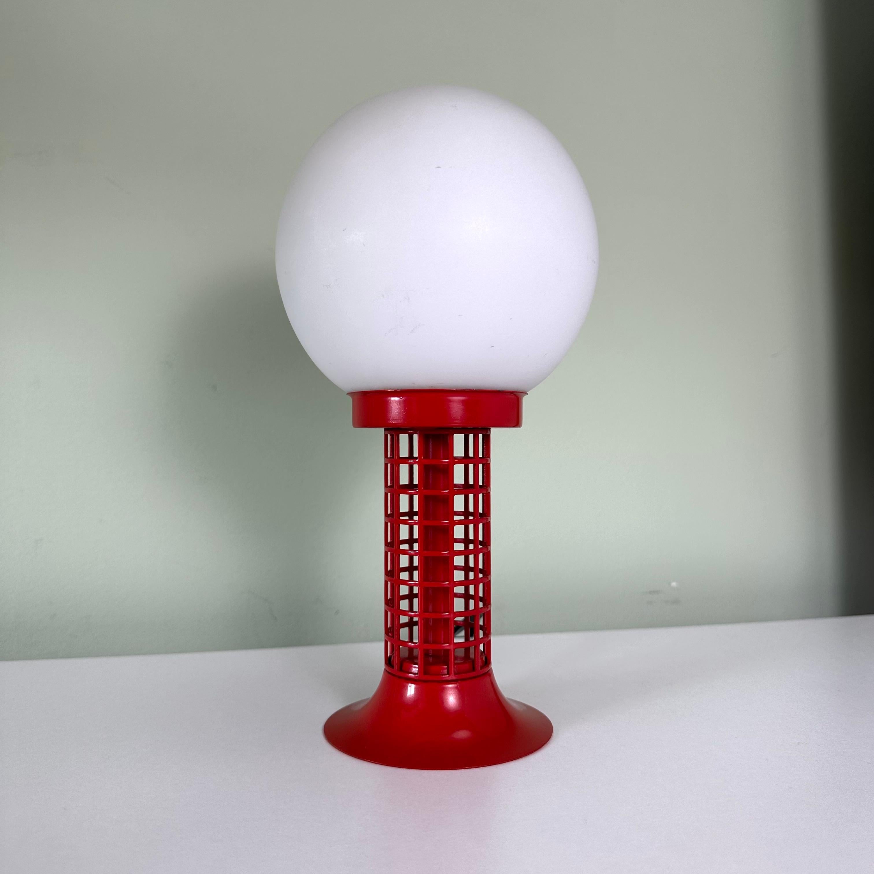 This is a single vintage 1970s table lamp with a modernist style with a white glass globe and a red metal base. Playing on primary colors in red and white, the top half of the lamp is an illuminated white frosted spherical glass globe shade,