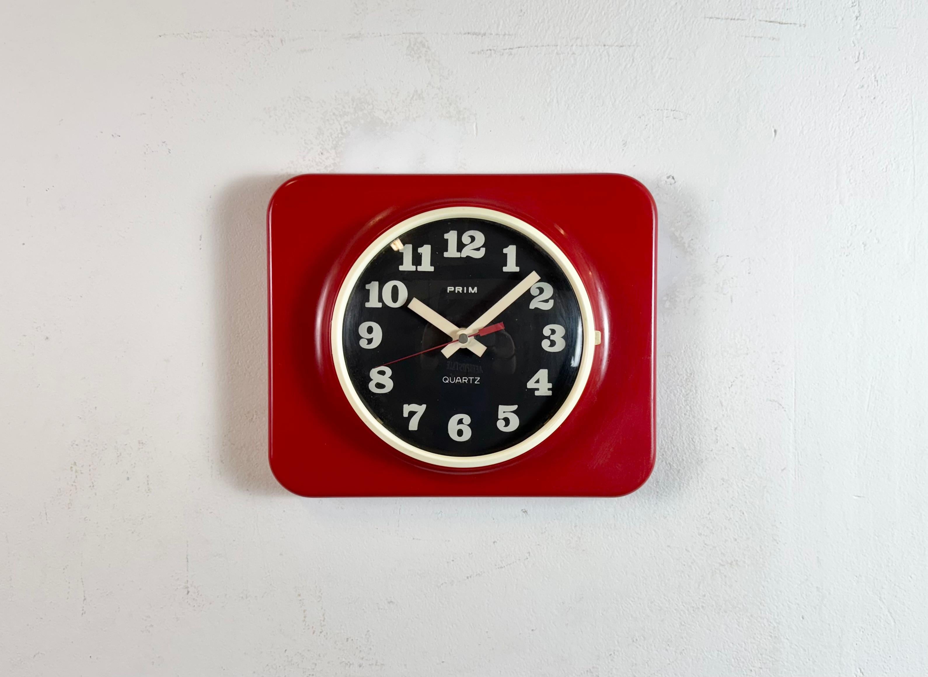 Vintage bakelite wall clock was made by Prim in former Czechoslovakia during the 1970s - 1980s. It features a red plastic body with black clockface and a convex clear glass cover. The original clockwork works perfectly and requires one C