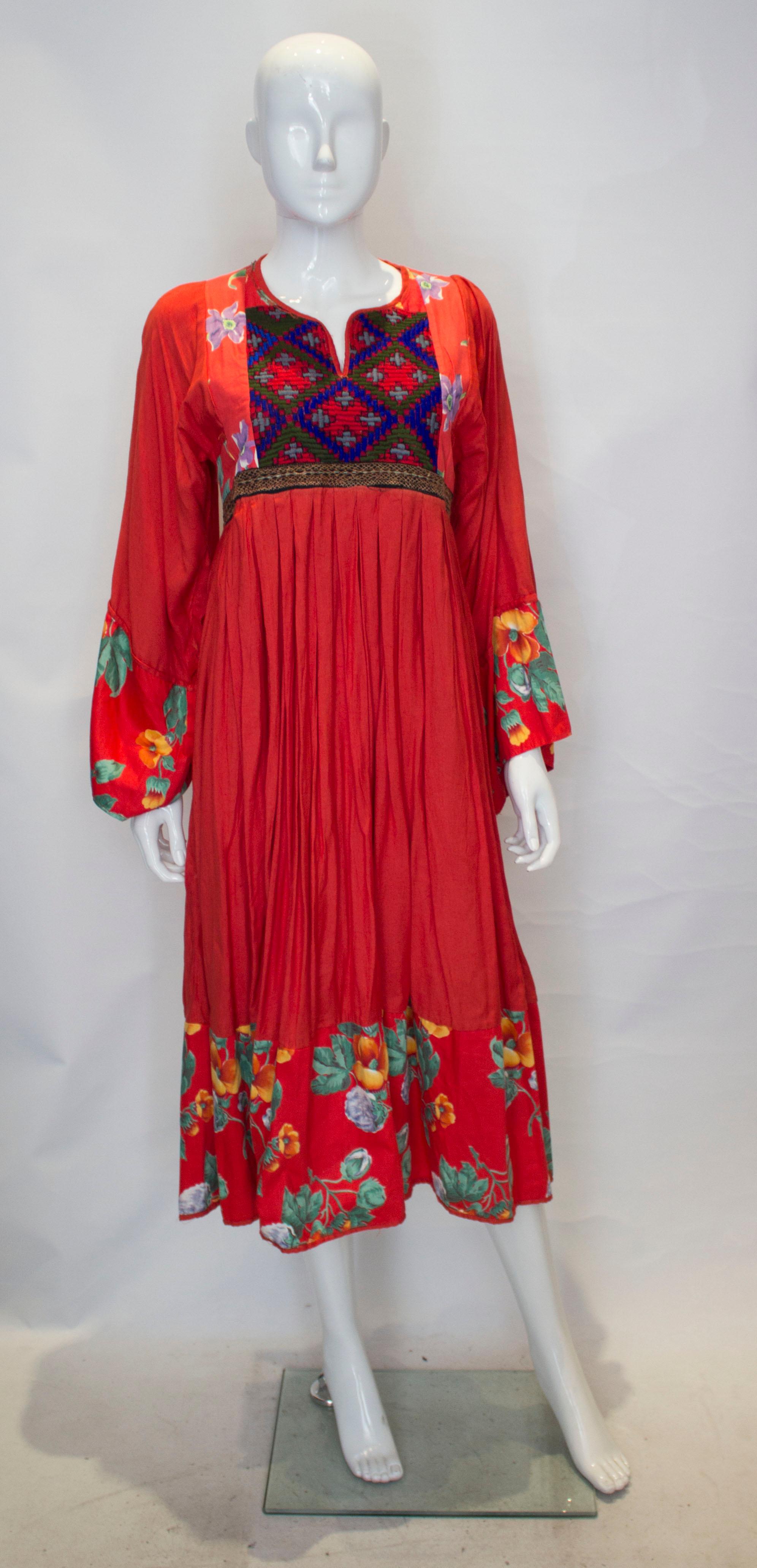 A fun easy to wear red cotton boho dress. The dress is collarless with a v neckline and has embroidery over the bust area with print cuffs  and hem.