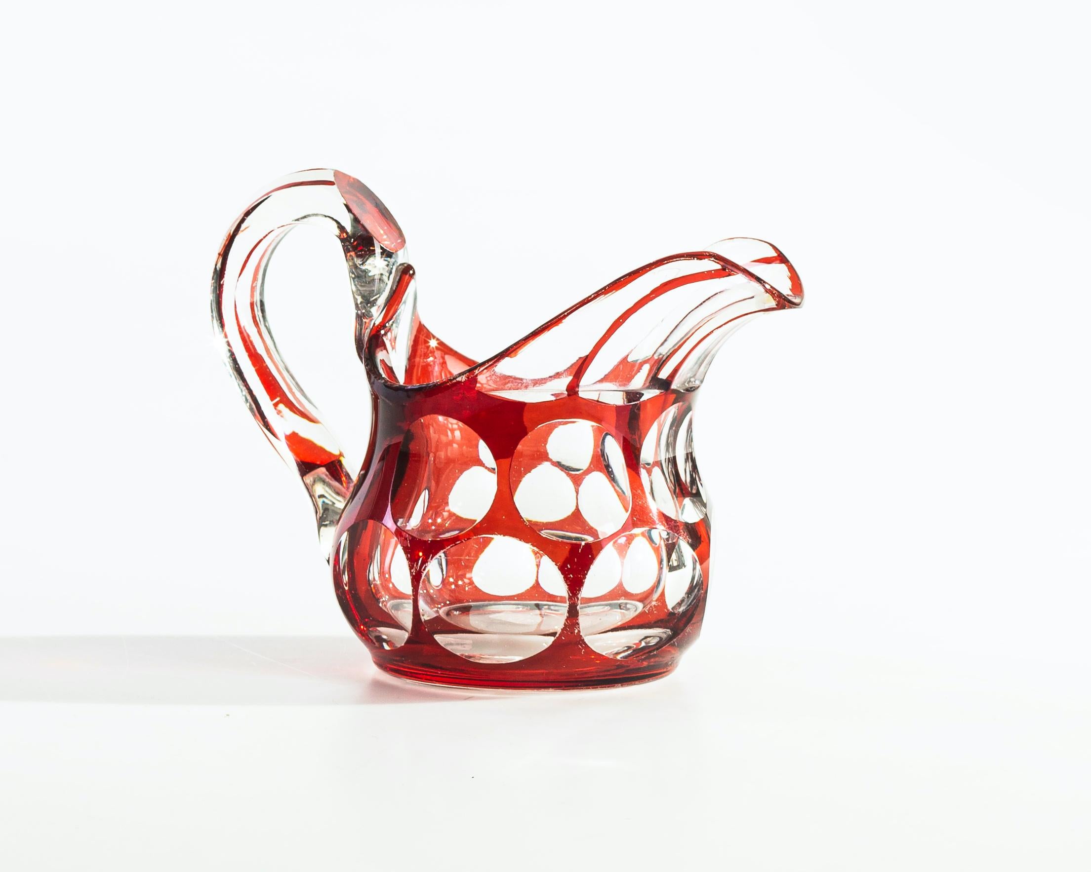 Red milk jug is an original decorative object realized in Europe in the 20th century. 

Precious jug in Rubin-colored glass and transparent circle decorations.