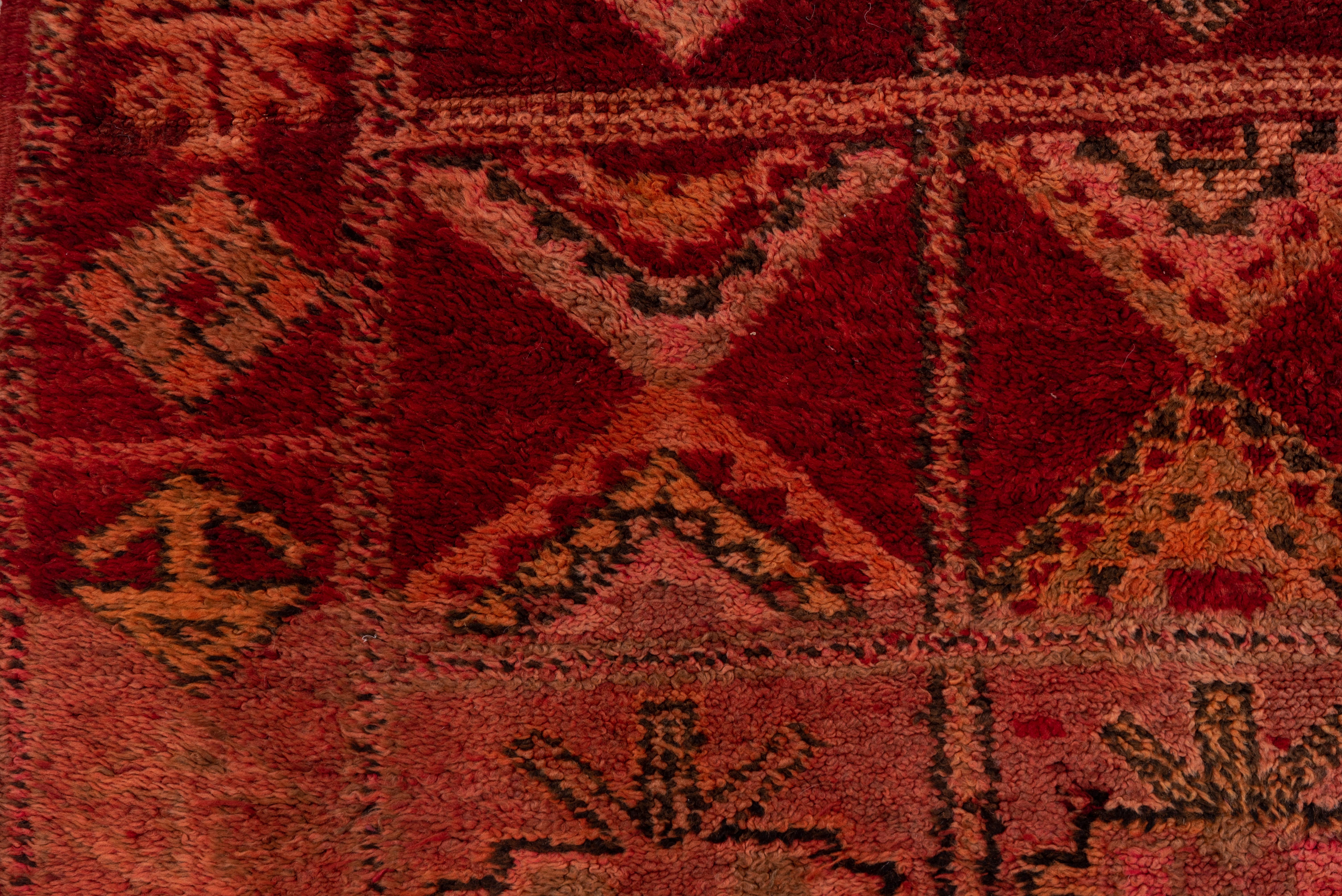 This Moroccan rug has a four by nine square lattice encloses smaller squares, lozenges, diamonds, stepped crosses, four anchor arrays, asterisk-stars and X's, detailed in straw, sand, blue-grey, goldenrod and red on a markedly abrashed red ground.