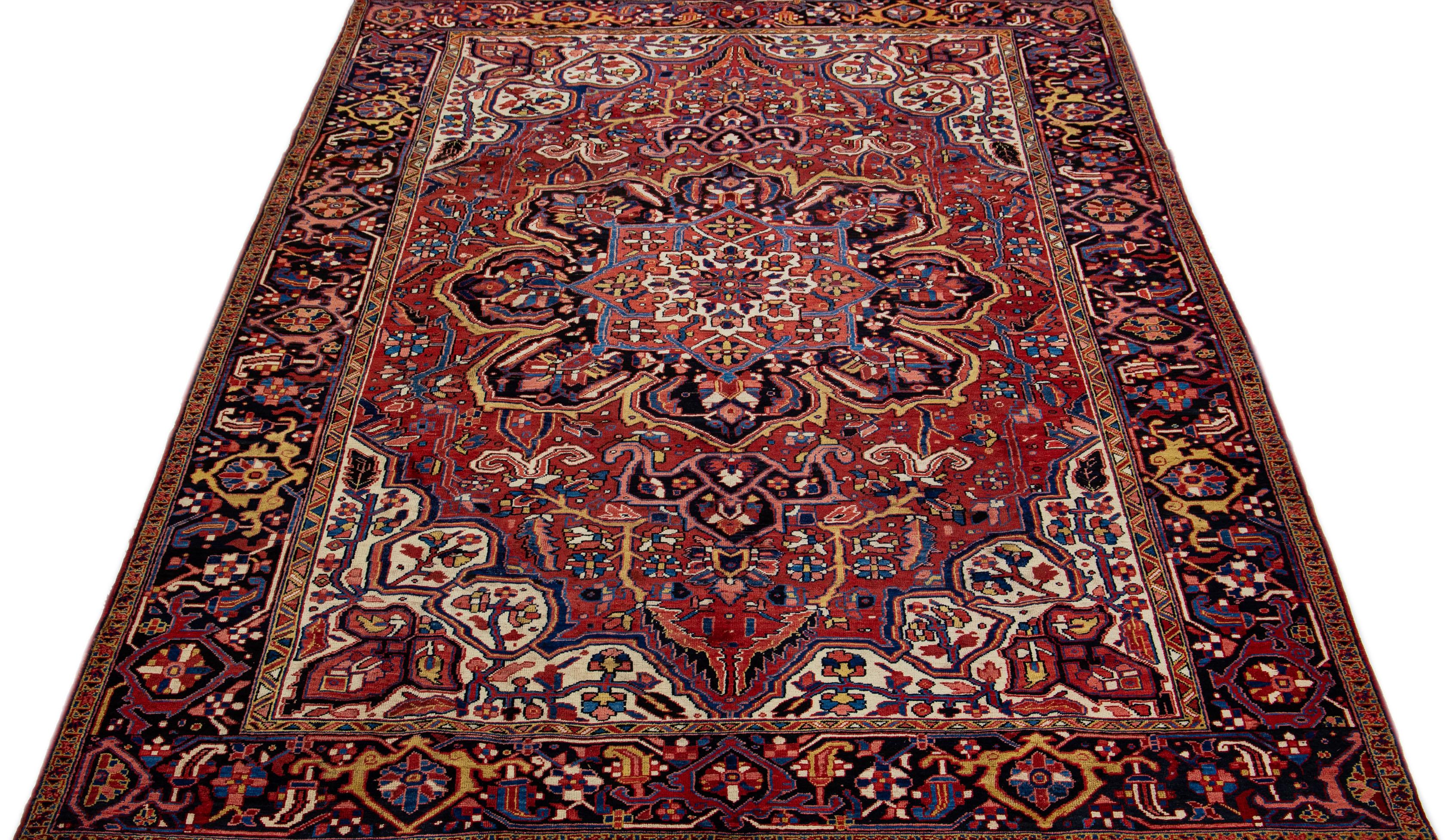 This is a stunning vintage Persian Heriz rug, artfully handcrafted using wool and featuring a vibrant red color field. The rug boasts an attractive dark blue frame with bright accents, cleverly arranged in an all-over geometric medallion pattern