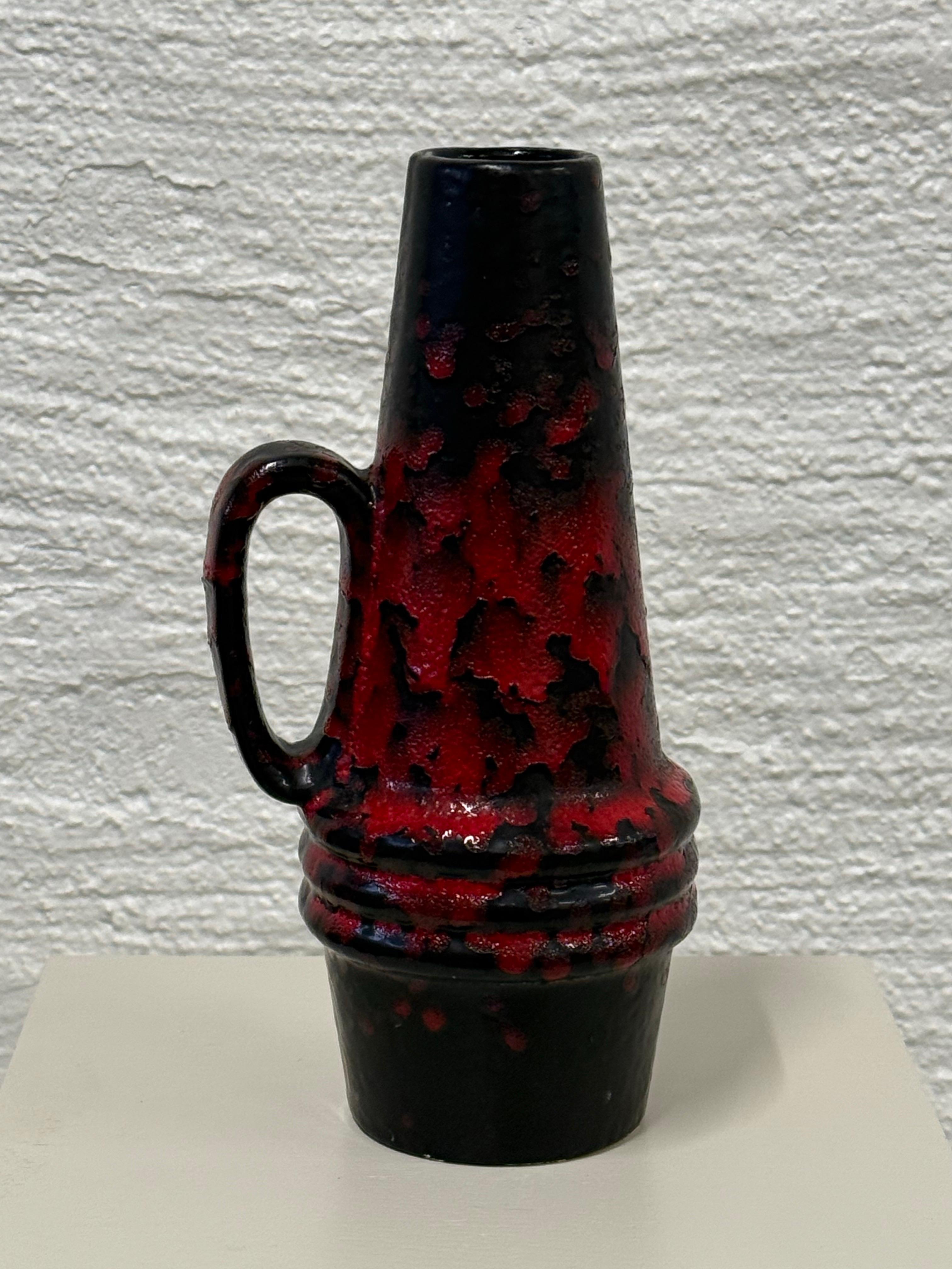 Aggiungi un tocco di charme di metà secolo ai tuoi interni con questo straordinario vaso in ceramica Scheurich, proveniente dalla Germania occidentale. Caratterizzato da un audace smalto lavico rosso e nero, questo pezzo mostra lo stile iconico e la