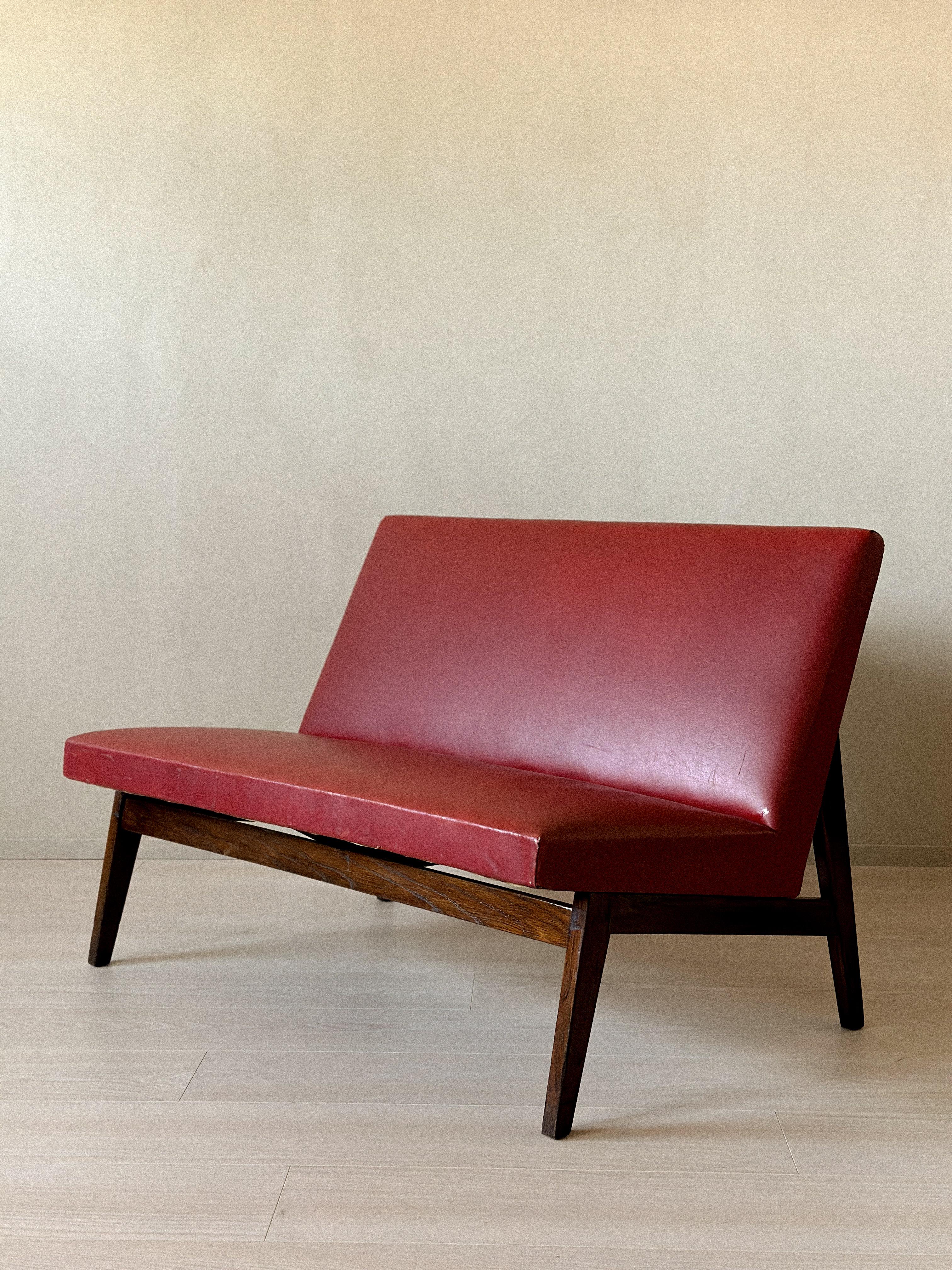 Vintage Red Skai Settee in the Style of Pierre Jeanneret, 1950s. Upholstered in original red skai from the 1950s. Dark stained wooden feet. Wear consistent with age and use, including marks and surface wear.