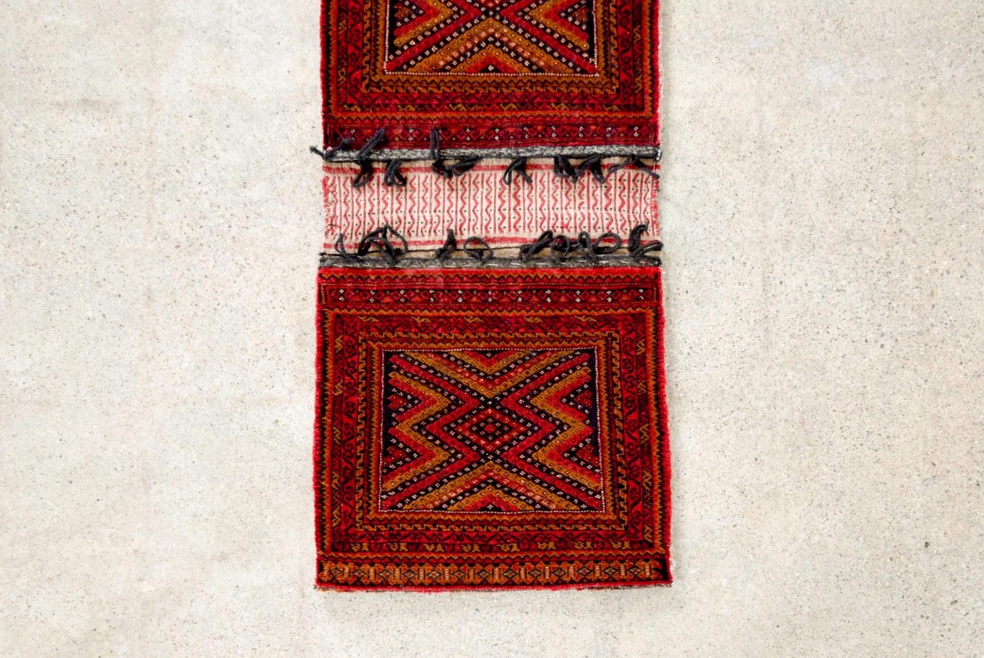 This authentic vintage Baluch tribal saddlebag rug is from a region near present-day Afghanistan and Pakistan. This small expertly handcrafted rug is connected by flat woven kilim with suspension loops and features an intricate geometric tribal