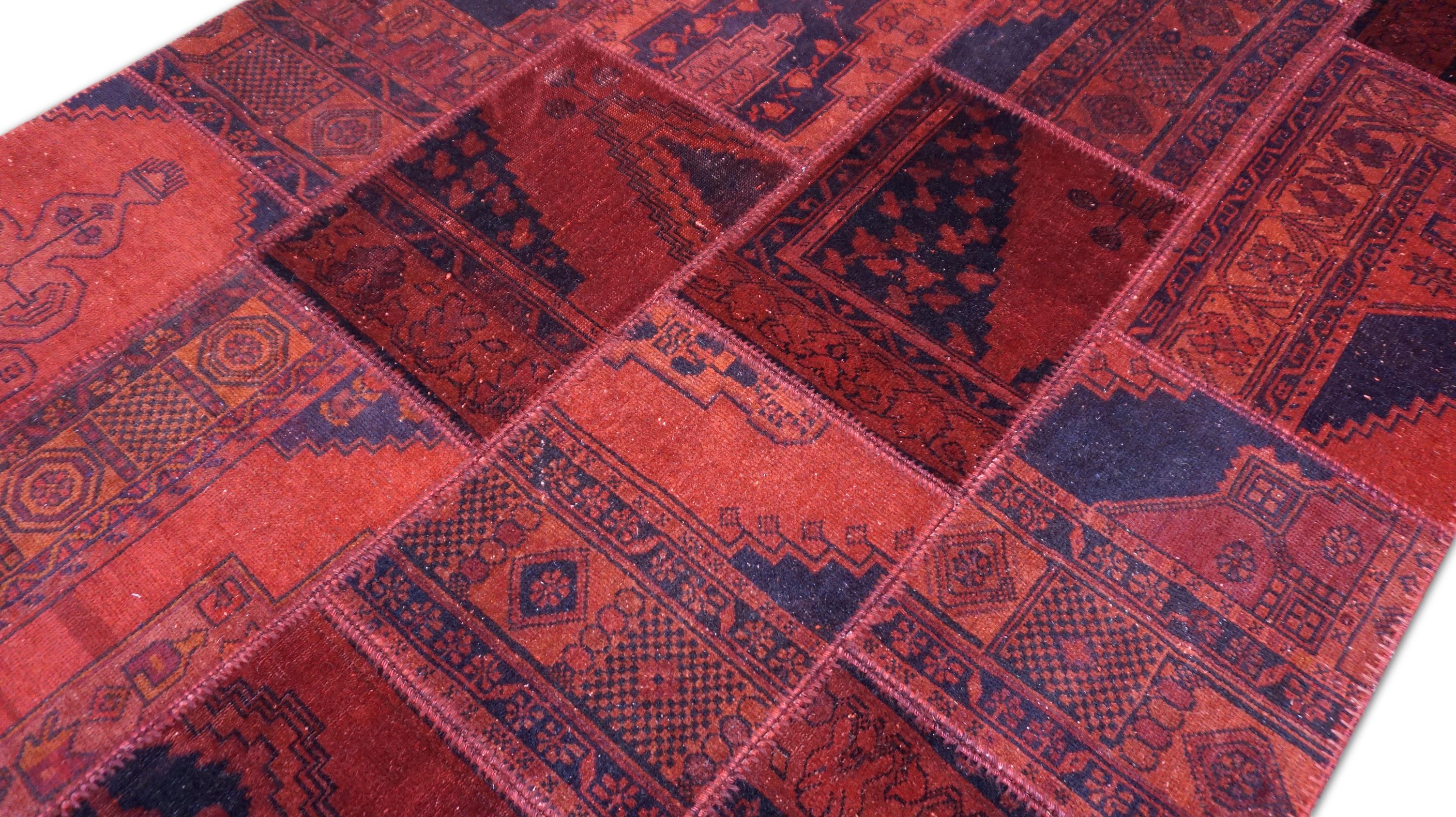 Dieser auffällige, handgewebte Wollflickenteppich ist eine einzigartige Vintage-Komposition, die die reichen Textiltraditionen feiert. Dieser Teppich wird aus sorgfältig ausgewählten Fragmenten von Stammesteppichen aus dem frühen 20. Jahrhundert