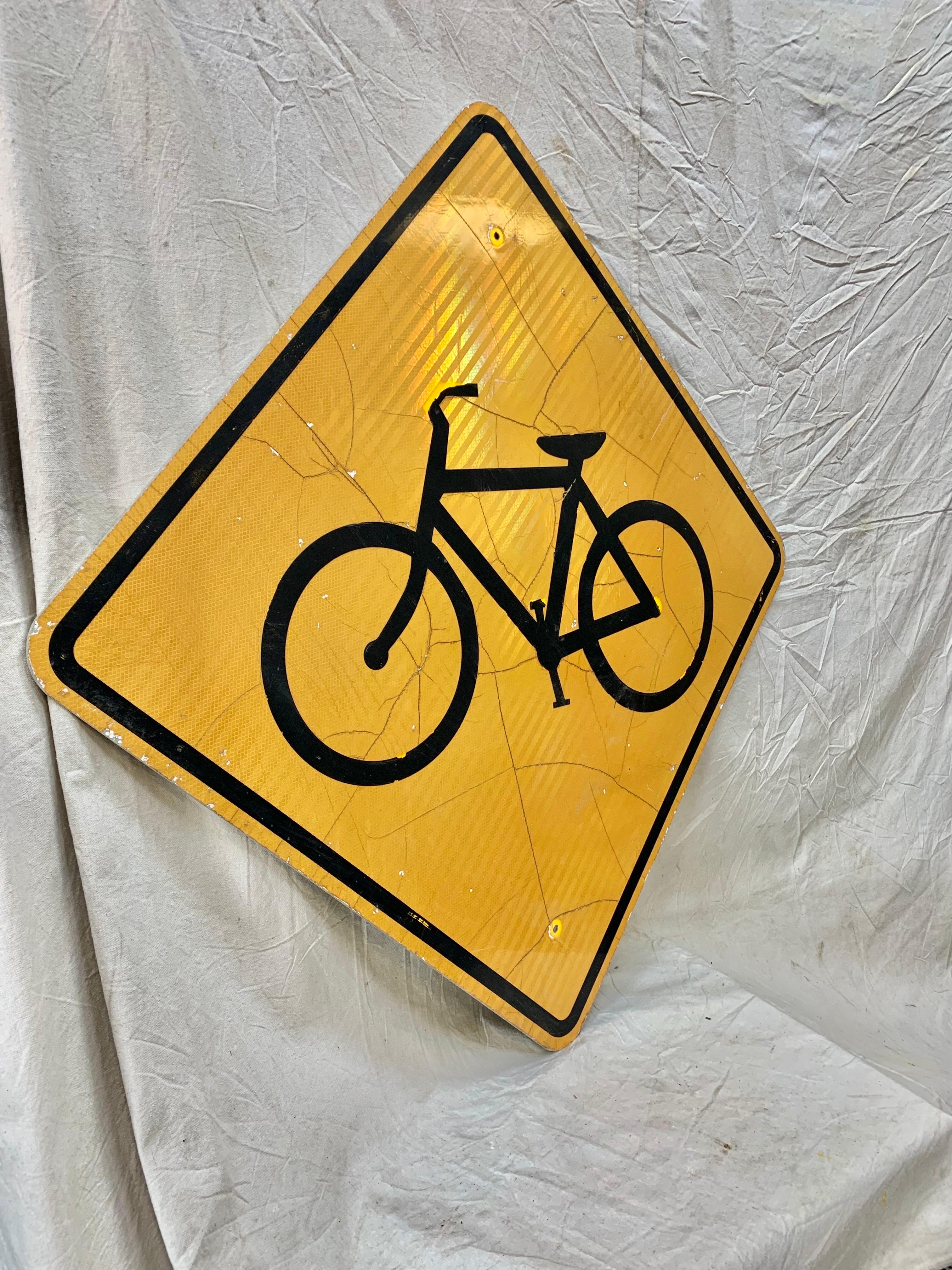 Dieses reflektierende Straßenschild im Vintage-Stil zeigt ein schwarzes Fahrrad auf gelbem Hintergrund. Dieses Schild wurde einst als Straßenschild verwendet, um die Autofahrer auf die Radfahrer in der Gegend aufmerksam zu machen, und weist eine