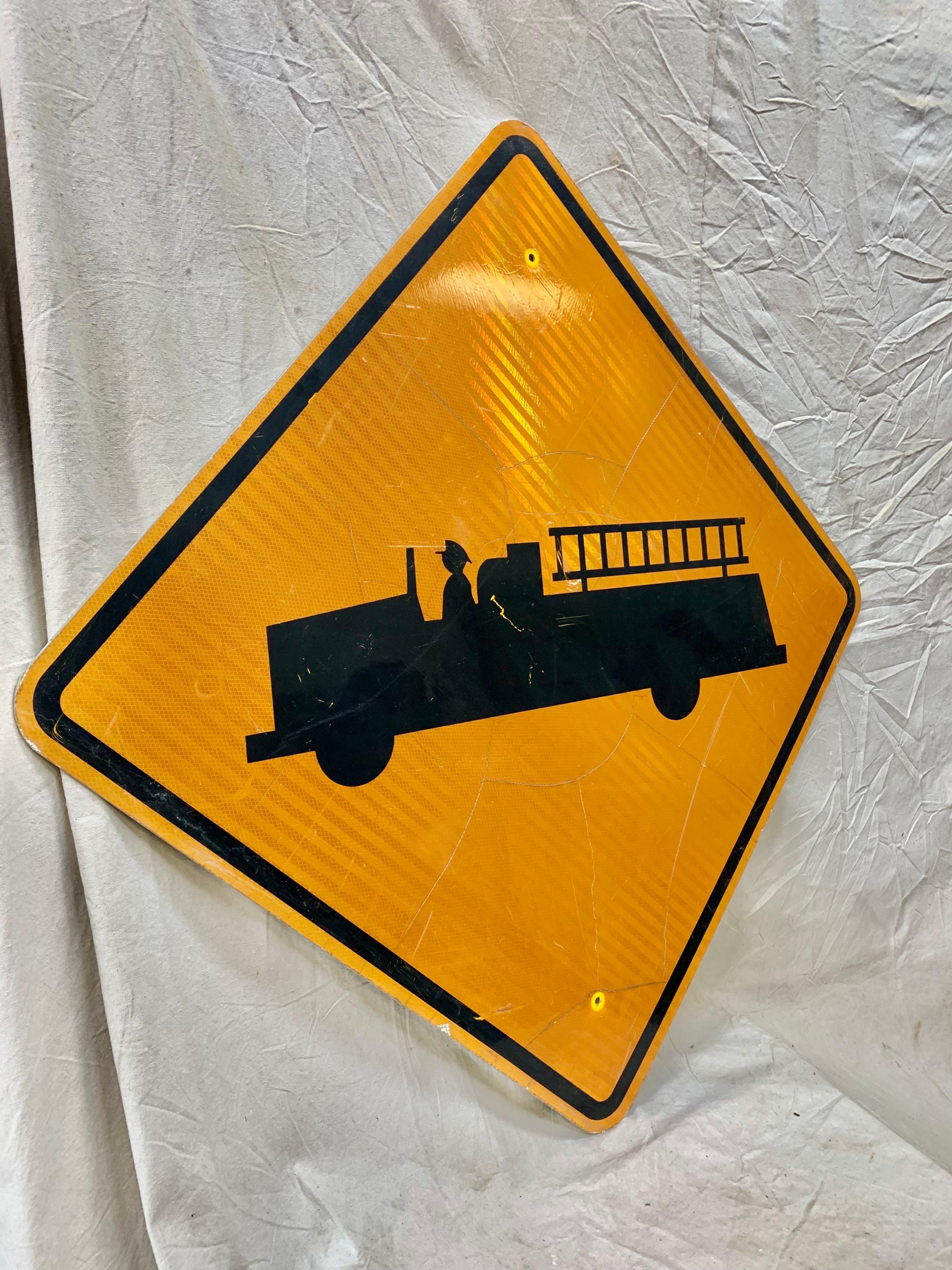 This Vintage Reflective Road Sign depicts a black firetruck with a yellow background. Once used as a street sign to inform motorist of firetrucks entering and exiting the highway, this sign presents great coloring, subject matter and patina. Today