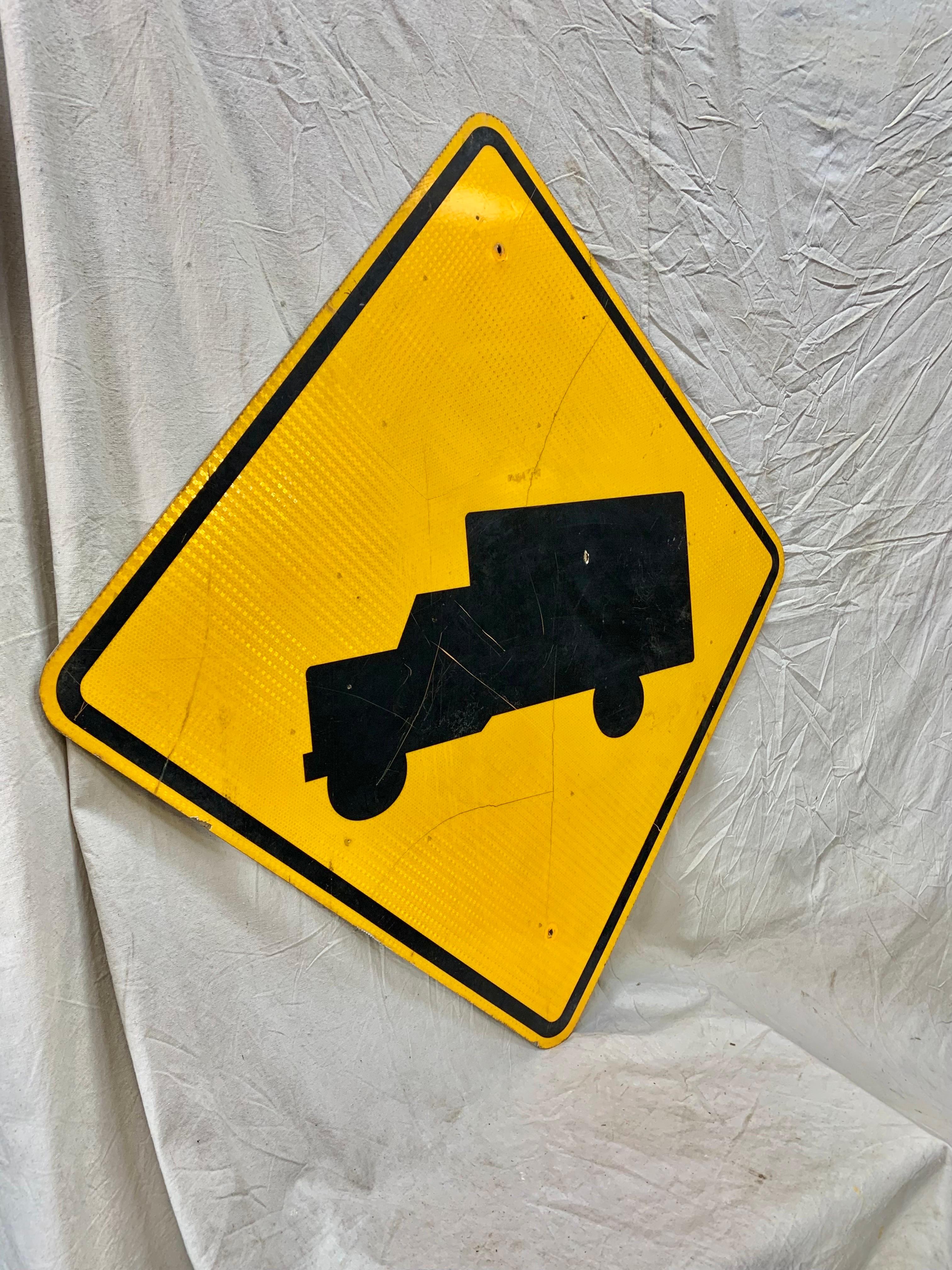 This Vintage Reflective Road Sign depicts a black truck with a yellow background. Once used as a street sign to inform motorist of trucks entering and exiting the highway, this sign presents great coloring, subject matter and patina. Today these