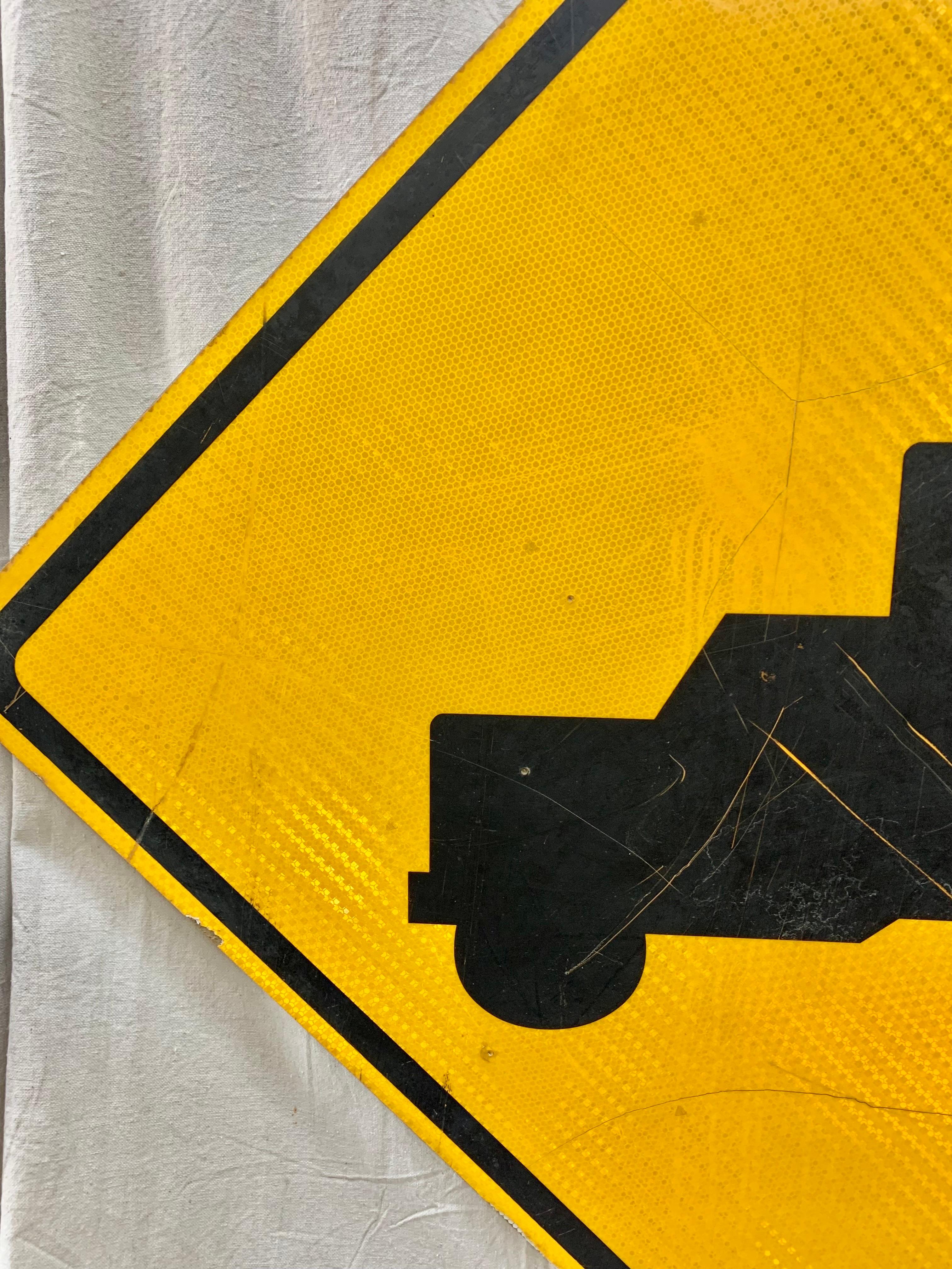 a yellow diamond-shaped sign with a black picture of a truck on it means