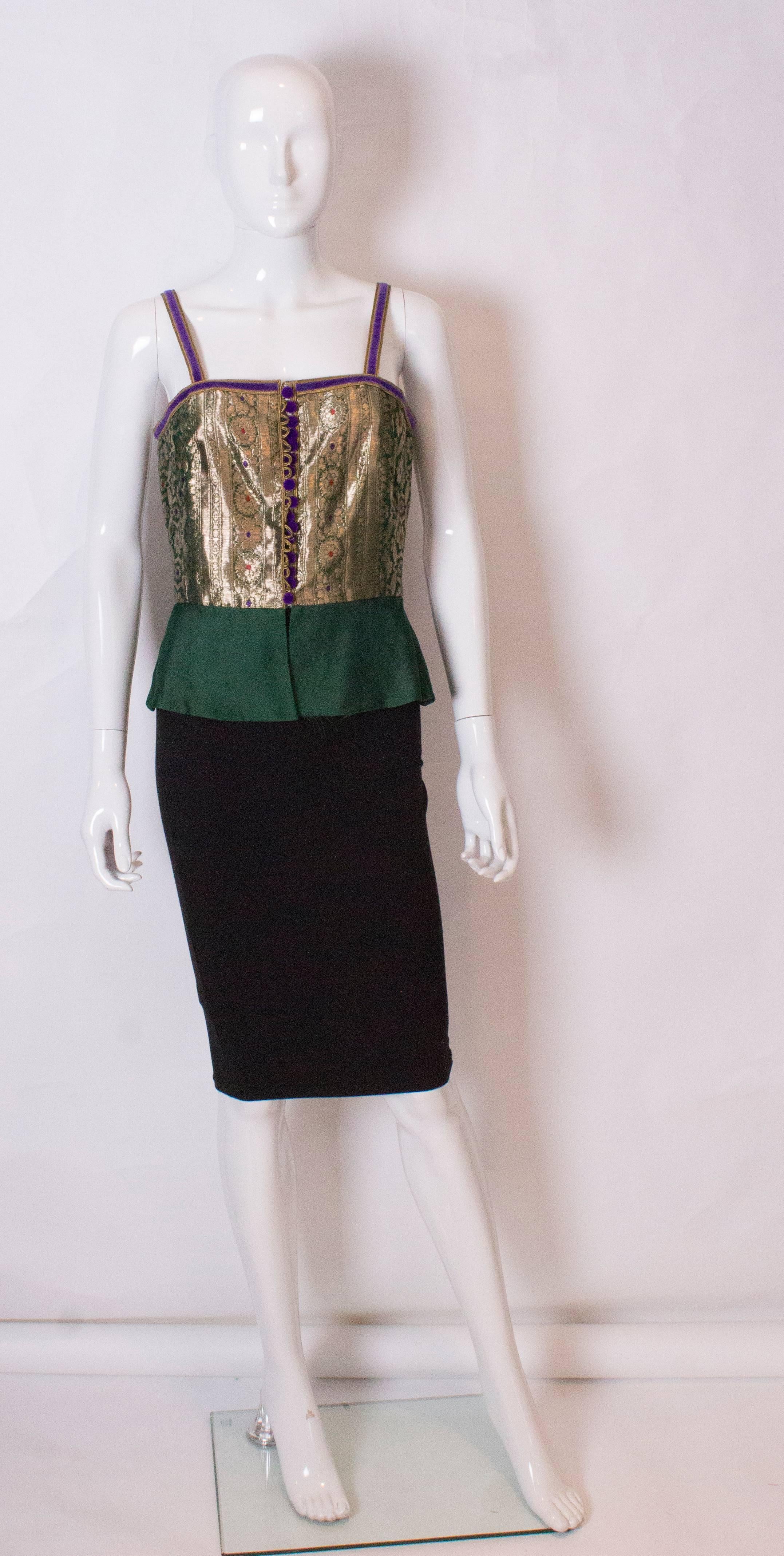 A chic vintage bodice by Regamus London. The body of the bodice is gold lame with a floral print and velvet trim, shoulder straps and buttons. It has a 5'' deep green peplum, and is fully lined.