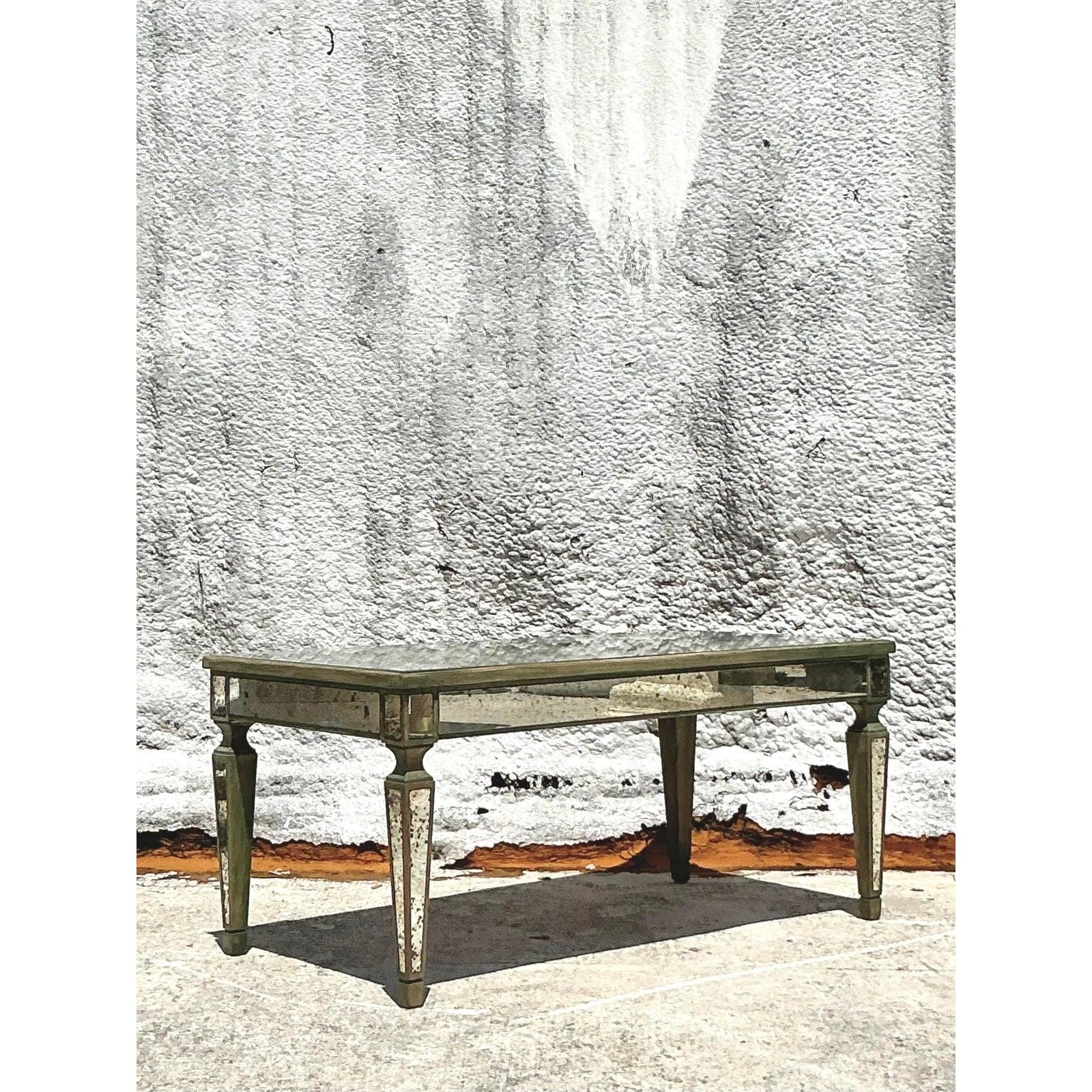Élevez votre espace de vie avec l'allure indéniable et la sophistication intemporelle de cette table basse à miroir antique Vintage Regency. Quintessence du glamour Hollywood Regency, son design présente de façon magistrale de vastes panneaux en