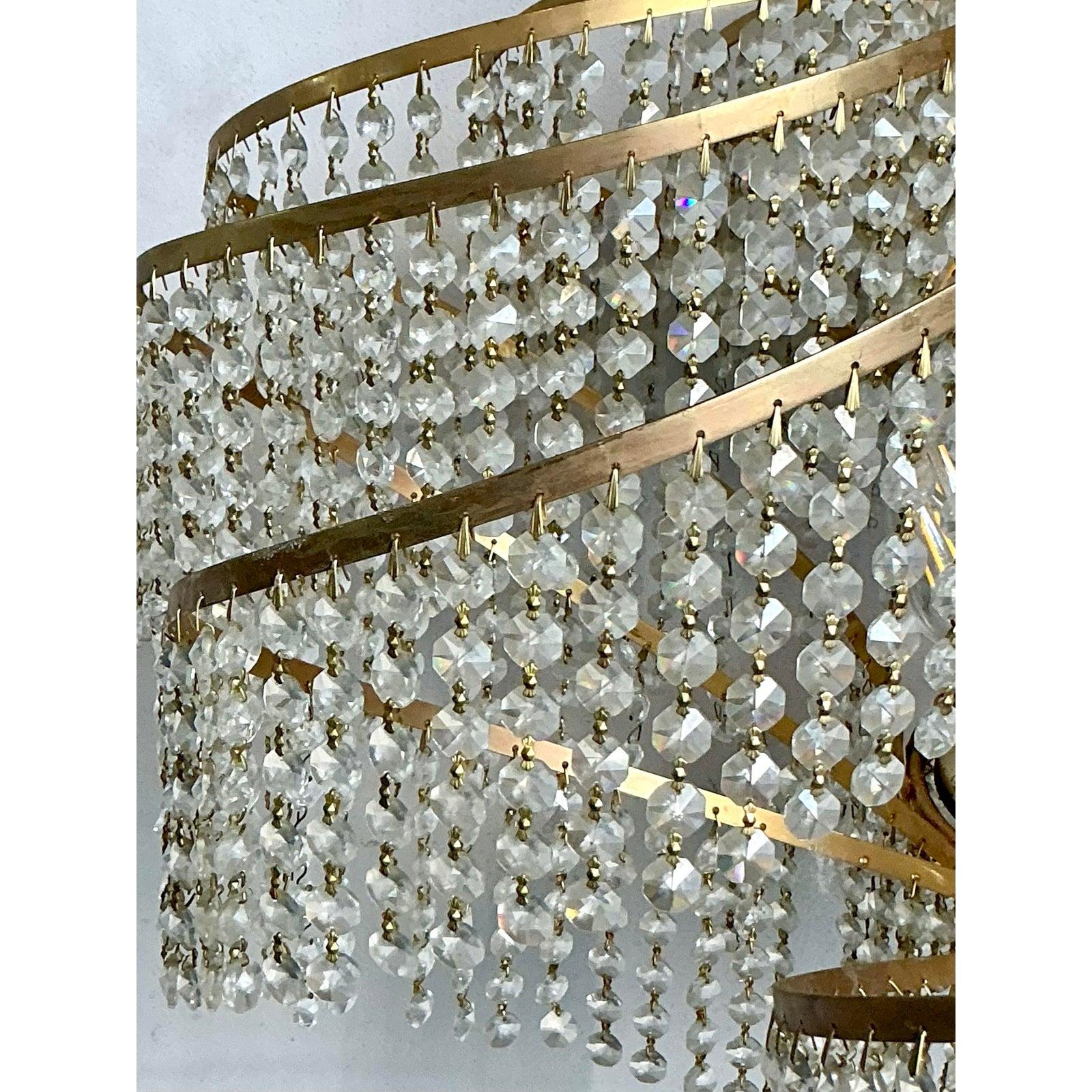 Questo splendido lampadario cattura l'opulento glamour dell'epoca Regency di Hollywood, fondendo perfettamente una decorazione massimalista con un dinamico design Mid-Century. L'apparecchio è caratterizzato da una struttura in metallo color ottone a
