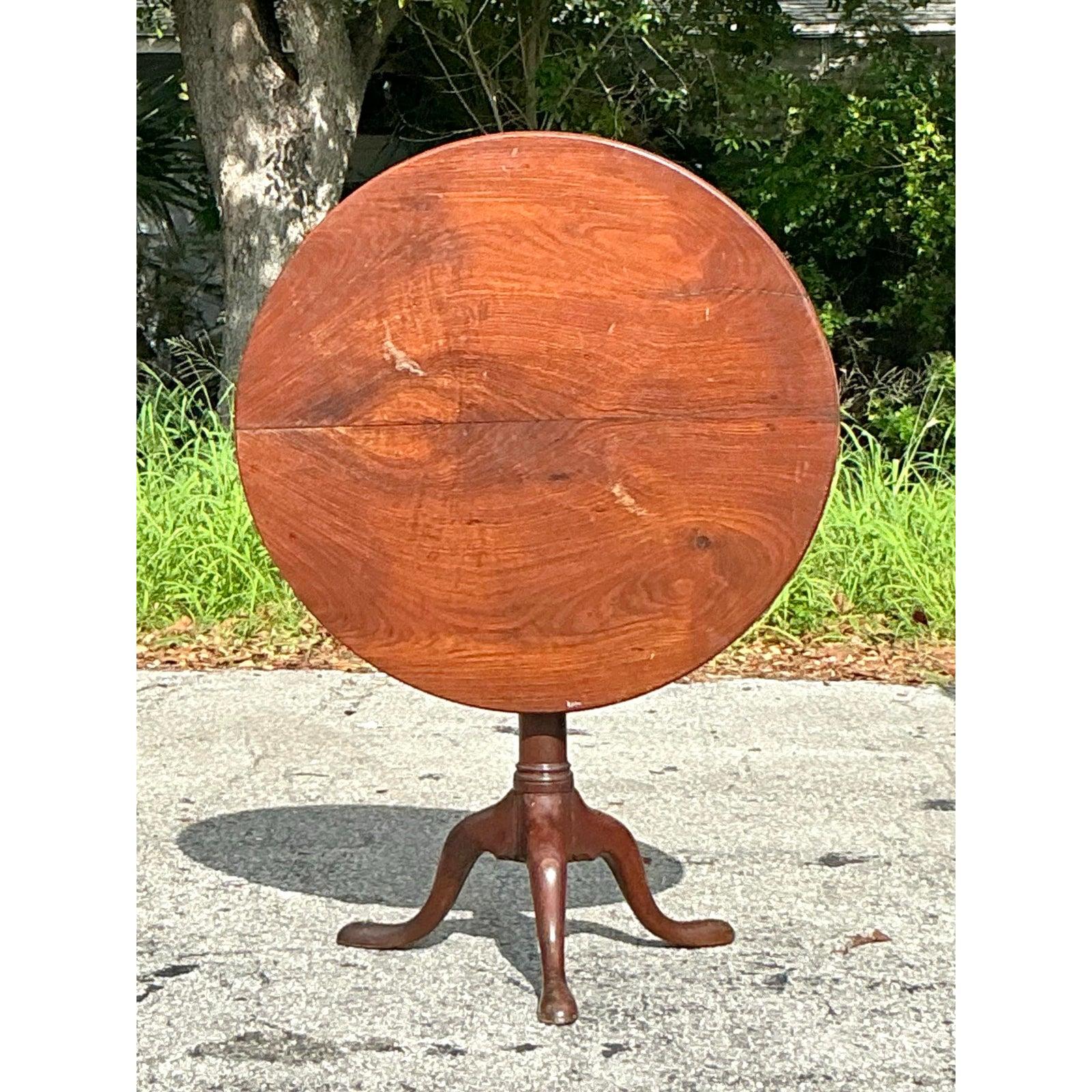 Discover the enduring elegance and ingenious functionality of this magnificent Vintage Regency Bookmatched Tilt Top Table. This exceptional piece features a beautifully rendered round top crafted from a rich, warm wood, where the grains are