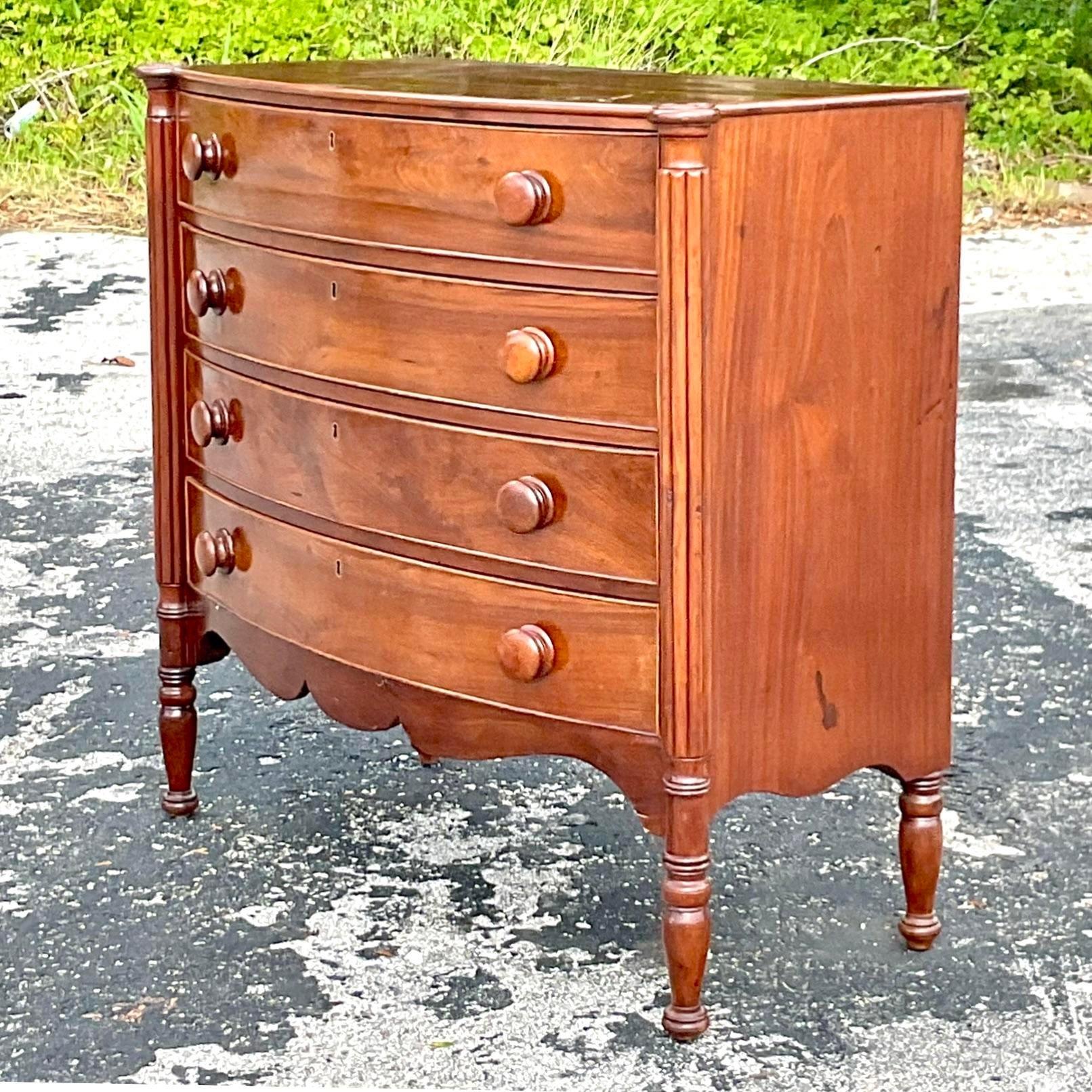 A stunning vintage Regency chest of drawers. A chic English mahogany bow front shape. Carved column detail at the corners. Acquired from a Palm Beach estate.