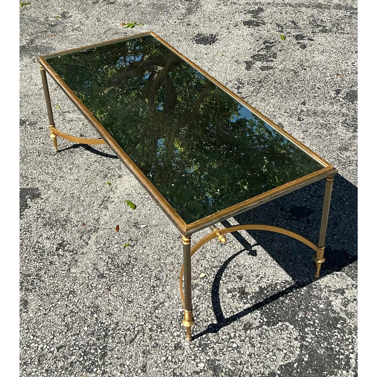 Cette exquise table basse vintage, inspirée par les célèbres designs de la Maison Jansen, respire l'élégance intemporelle de la Régence. Avec son cadre en laiton et en métal, ses pieds gracieusement effilés et son châssis incurvé, cette pièce