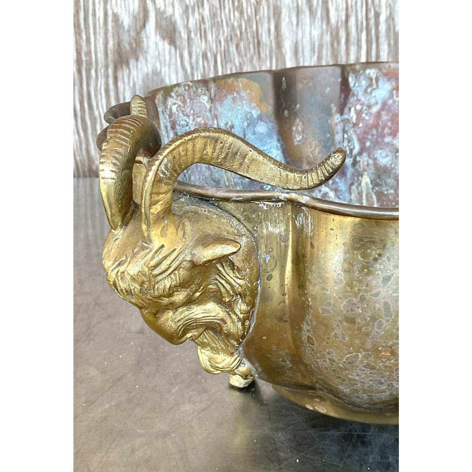 Fai una dichiarazione audace con questo Jardinière a testa d'ariete in ottone Vintage Regency, squisitamente dettagliato. Con il suo corpo smerlato e martellato a mano, le maniglie a testa d'ariete e la base a zampa d'asino, questo grande vaso