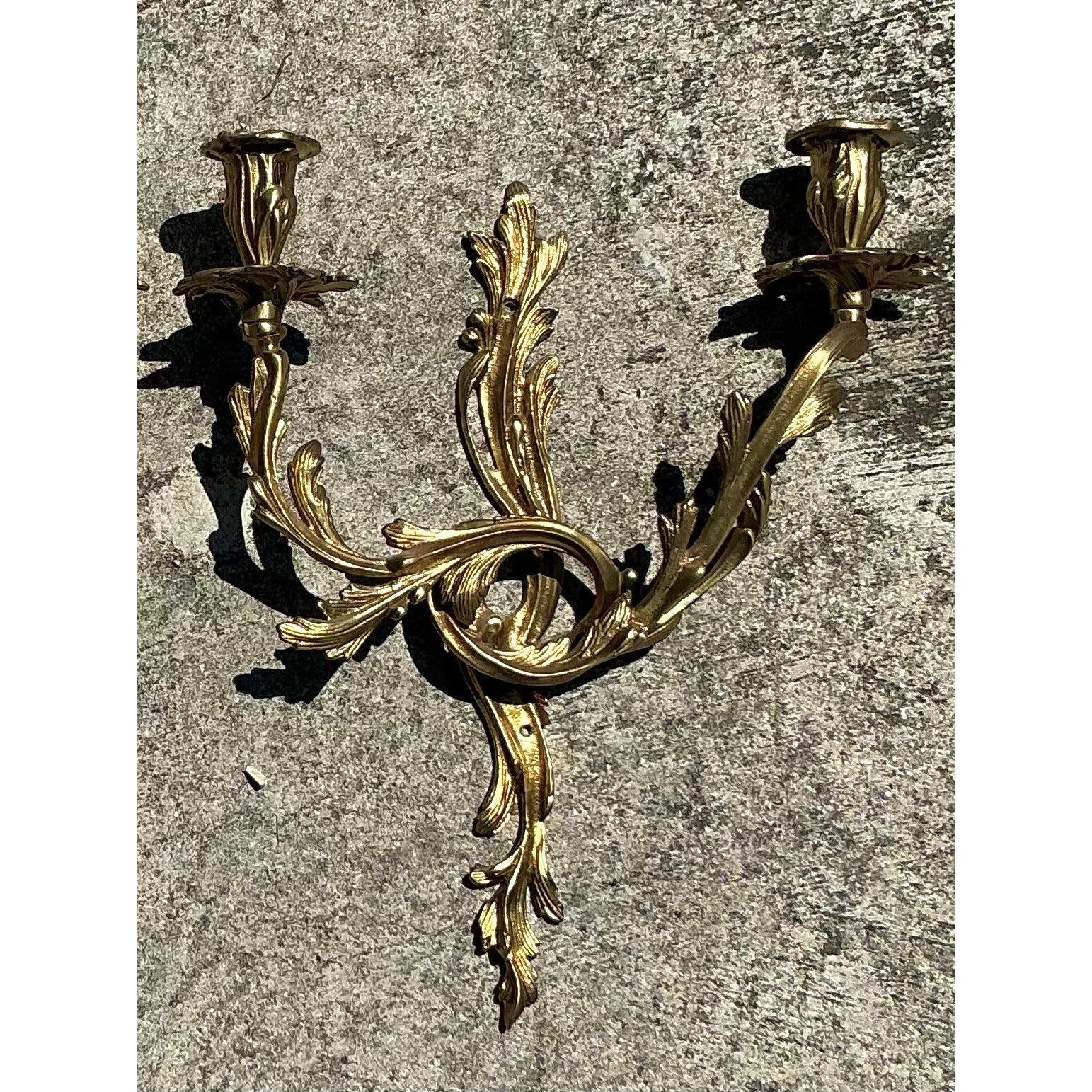 Cette paire d'appliques à bougie rococo en laiton de style Vintage Regency rehausse votre intérieur. Riches en détails ornementaux, ces appliques magnifiquement moulées présentent des feuilles d'acanthe enroulées et des courbes élégantes qui