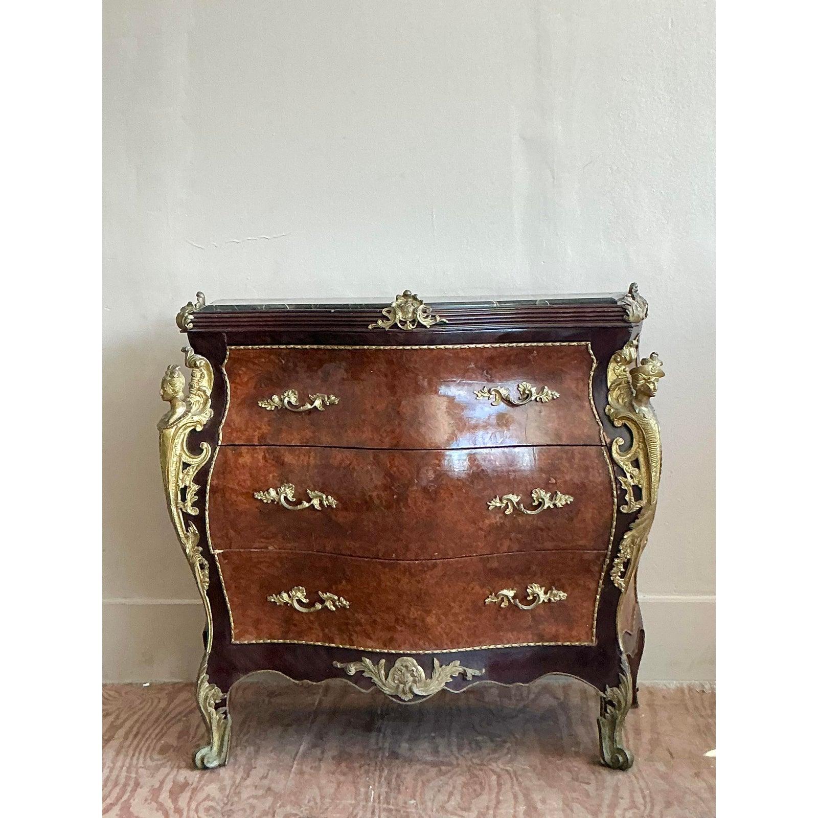 A masterpiece of Rococo exuberance, this exquisite vintage commode embodies the opulence and artistry of the Louis XV style. The chest features a graceful bombé silhouette, with sensuously curved drawer fronts showcasing luminous, book-matched burl