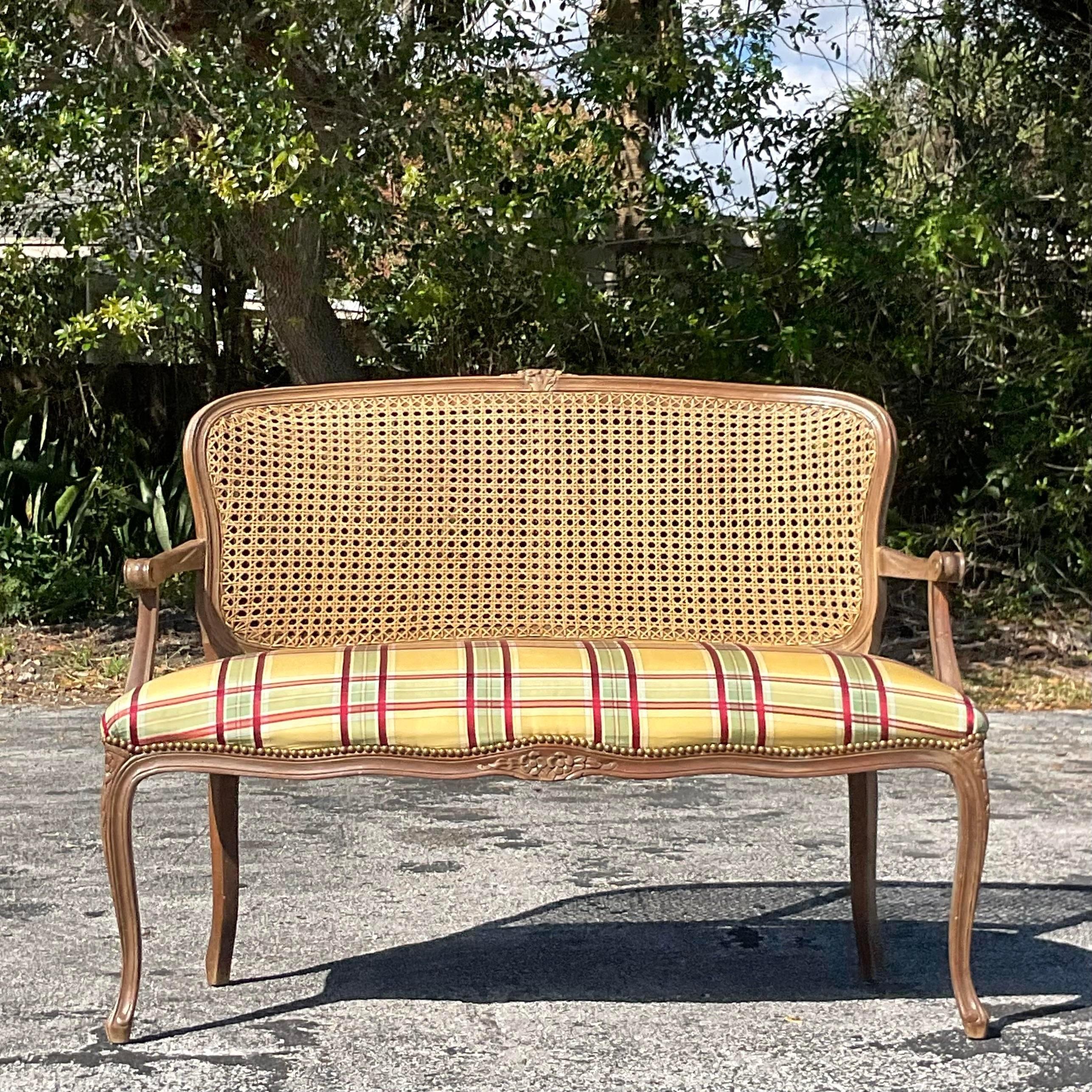 A fabulous vintage Regency settee. A china hand carved frame with amazing attention to detail. An inset cane back with a silk plaid upholstery. Acquired from a Palm Beach estate.