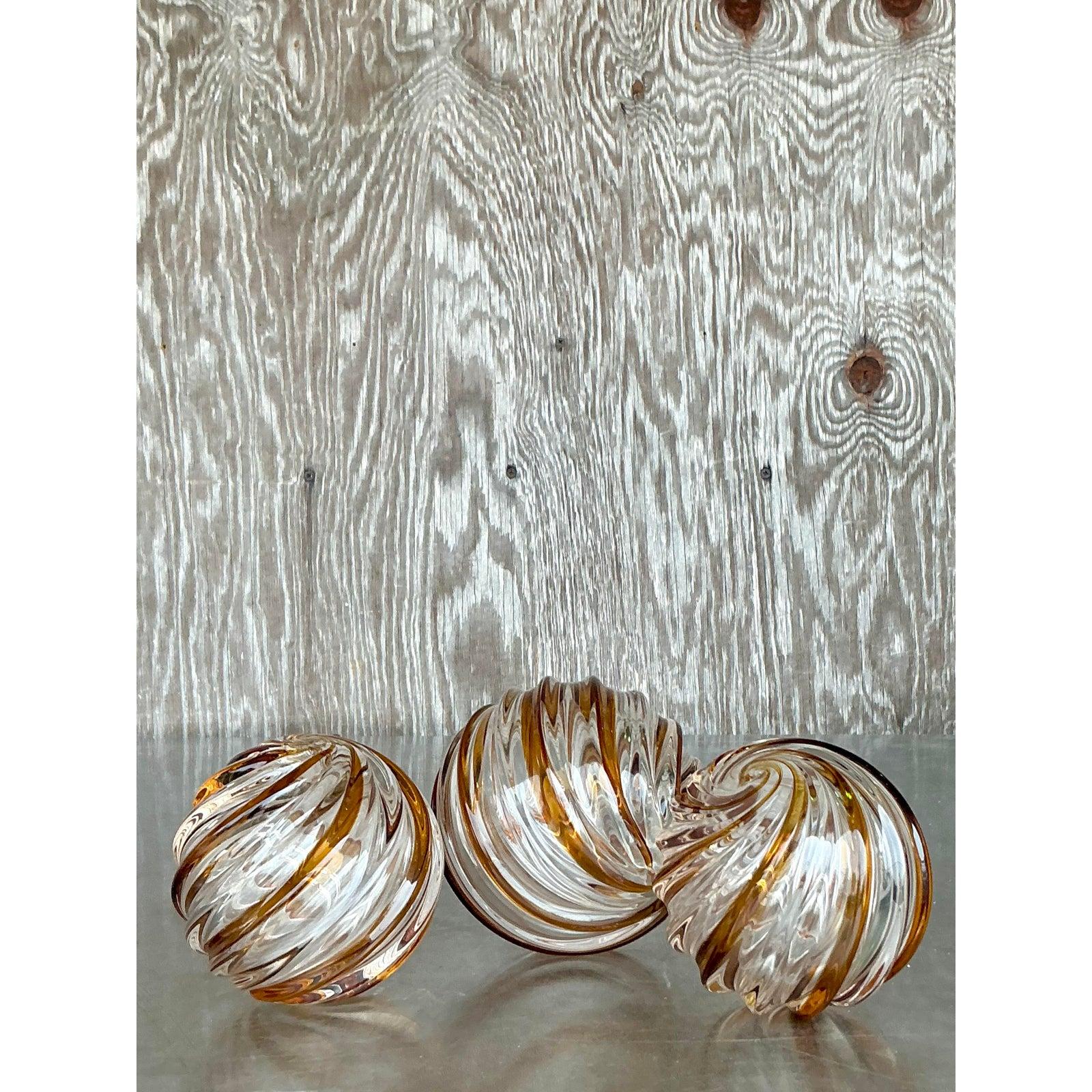 Aggiungi un tocco di stile sofisticato al tuo spazio con questo trio di sfere in vetro soffiato Vintage Regency Caramel Swirl. Queste sfere in vetro soffiato a mano sono caratterizzate da ipnotici nastri di vetro ambrato e trasparente, che catturano