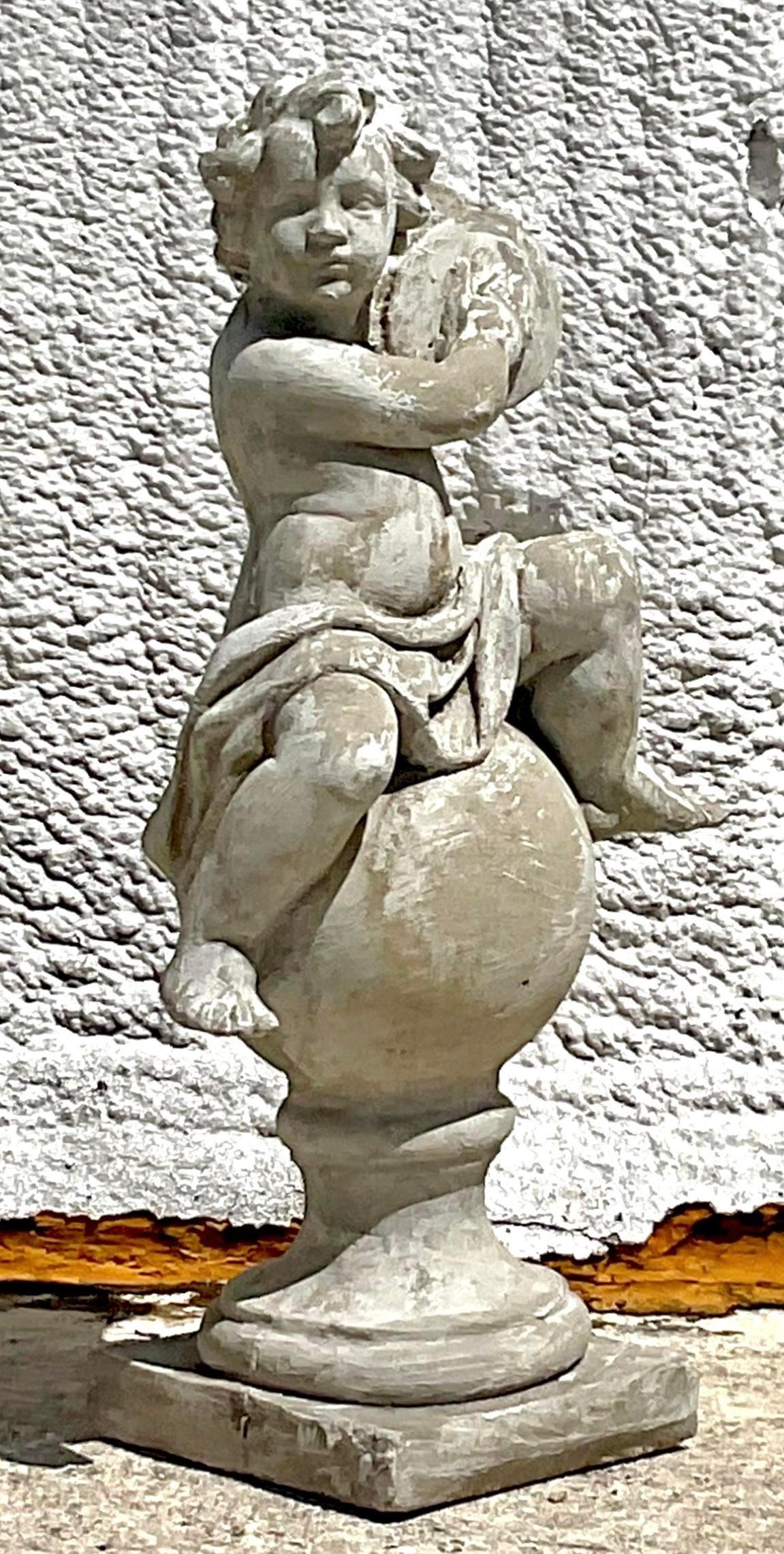Questa incantevole scultura figurata vintage Regency in cemento è caratterizzata da una stravagante rappresentazione di un cherubino seduto in cima a un piedistallo rotondo. Con la sua patina invecchiata e il suo design classico, questo pezzo emana