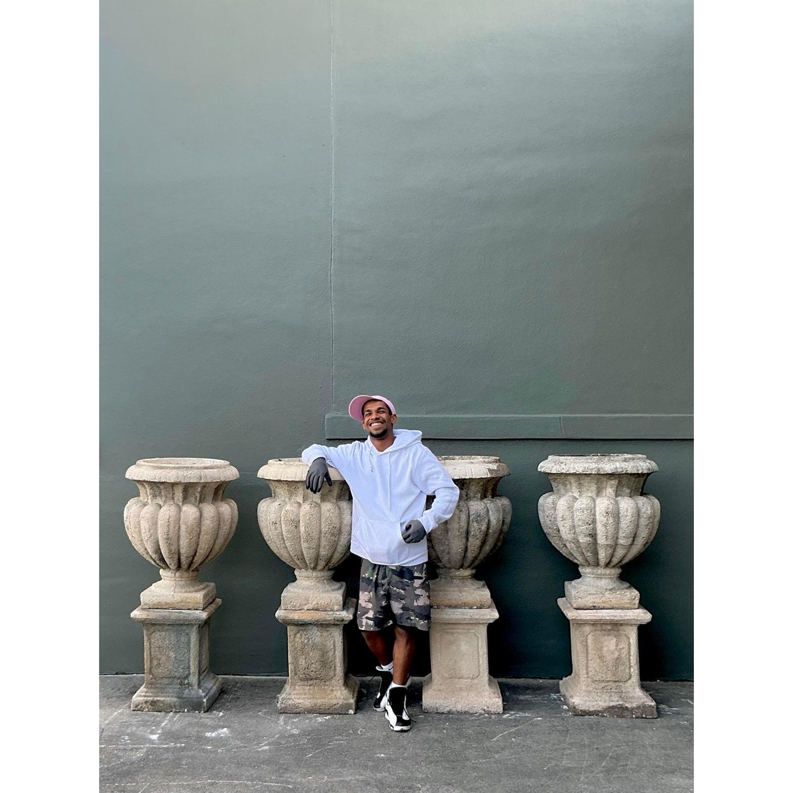 Command attention in your landscape or entryway with this monumental pair of vintage Regency-style cast concrete urns on pedestals. Expertly cast with classical proportions, each urn features a generous campana form adorned with deep, sculptural