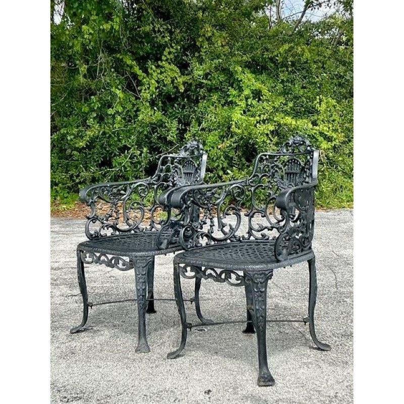 Évoquez l'élégance intemporelle d'un jardin à la française du XIXe siècle avec cette exquise paire de fauteuils en fonte vintage. Chaque chaise est une œuvre d'art, avec un dossier ajouré et orné, centré sur un motif de lyre lyrique, symbole